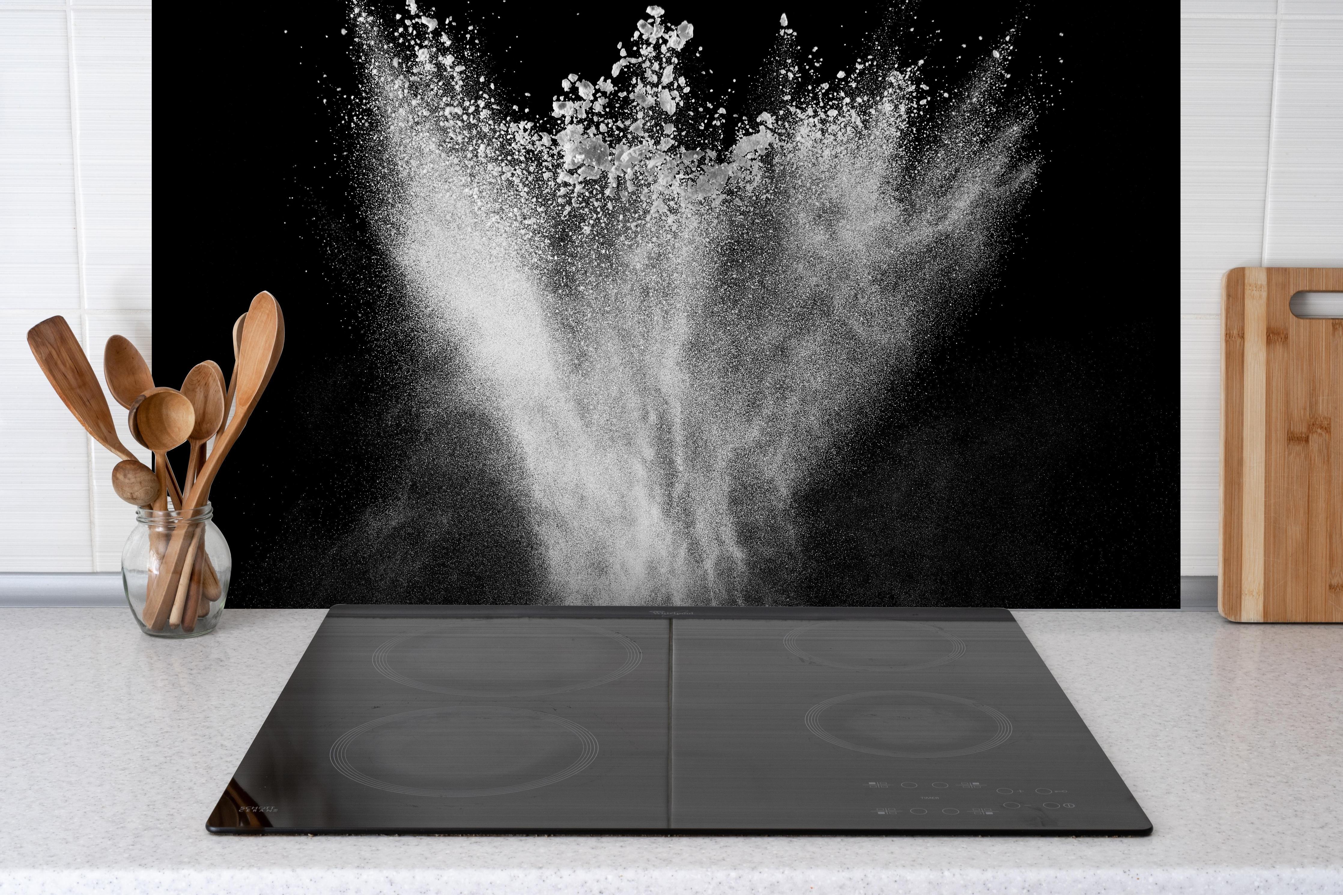 Spritzschutz - Pulver Explosion hinter einem Cerankochfeld zwischen Holz-Kochutensilien
