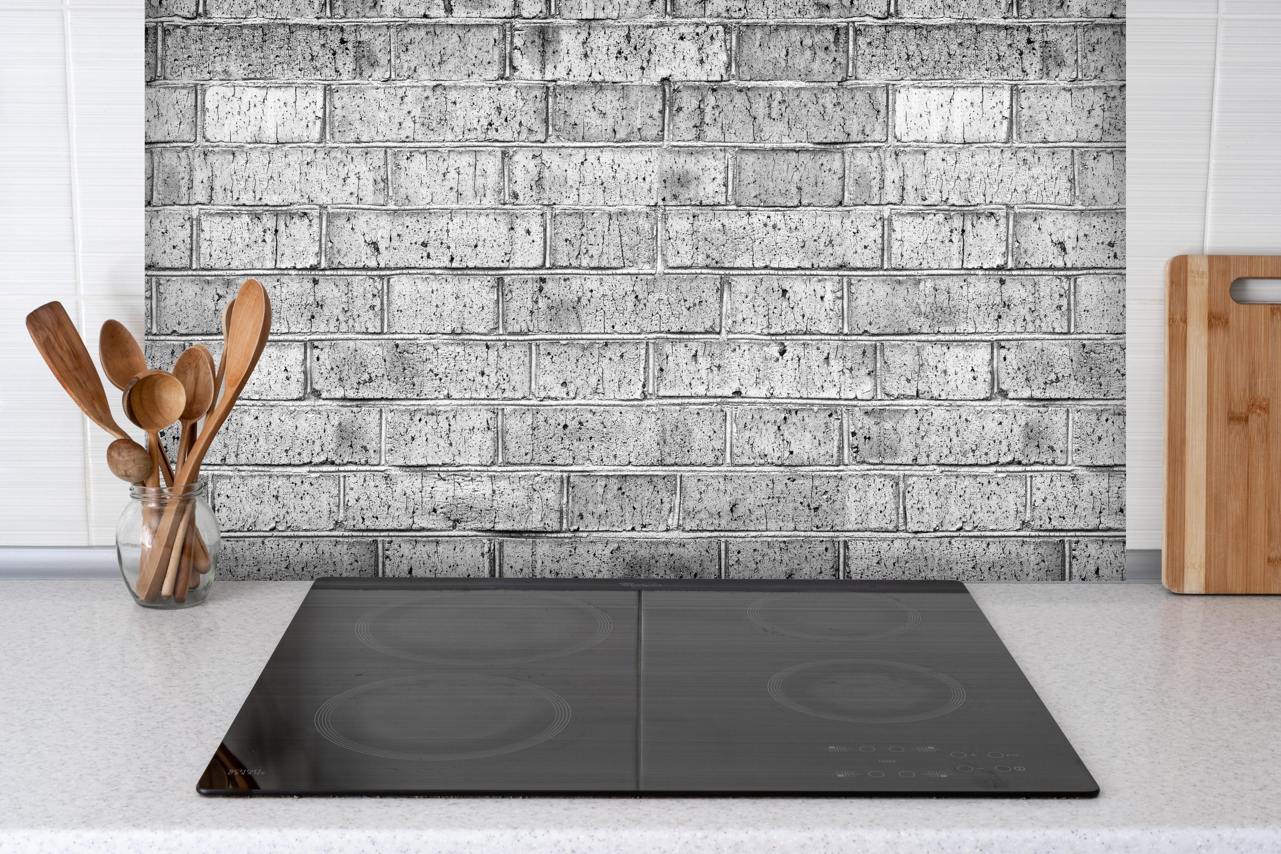 Spritzschutz - Raues hellgraues Mauerwerk hinter einem Cerankochfeld zwischen Holz-Kochutensilien
