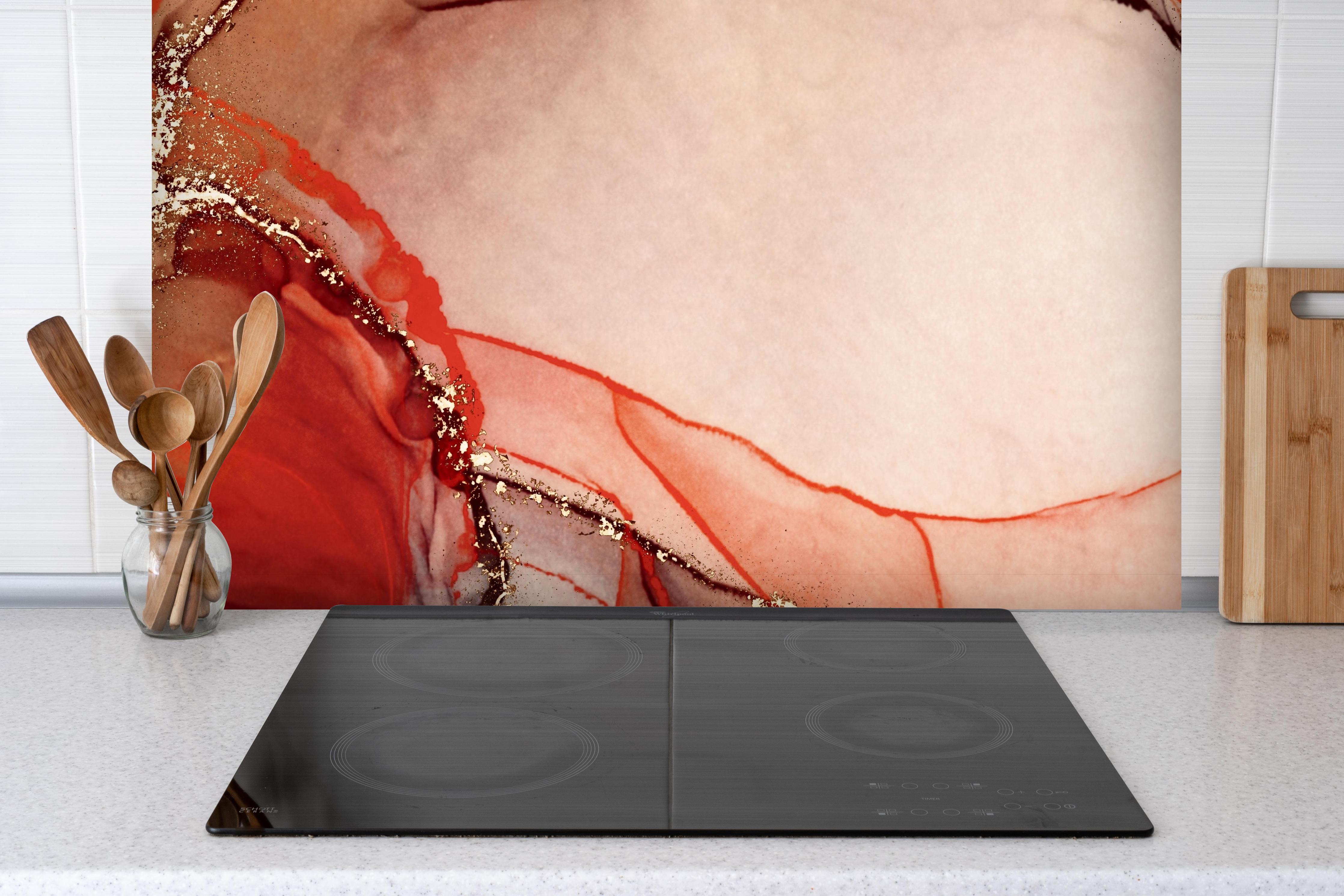 Spritzschutz - Rötliche Tinte mit Goldelementen hinter einem Cerankochfeld zwischen Holz-Kochutensilien
