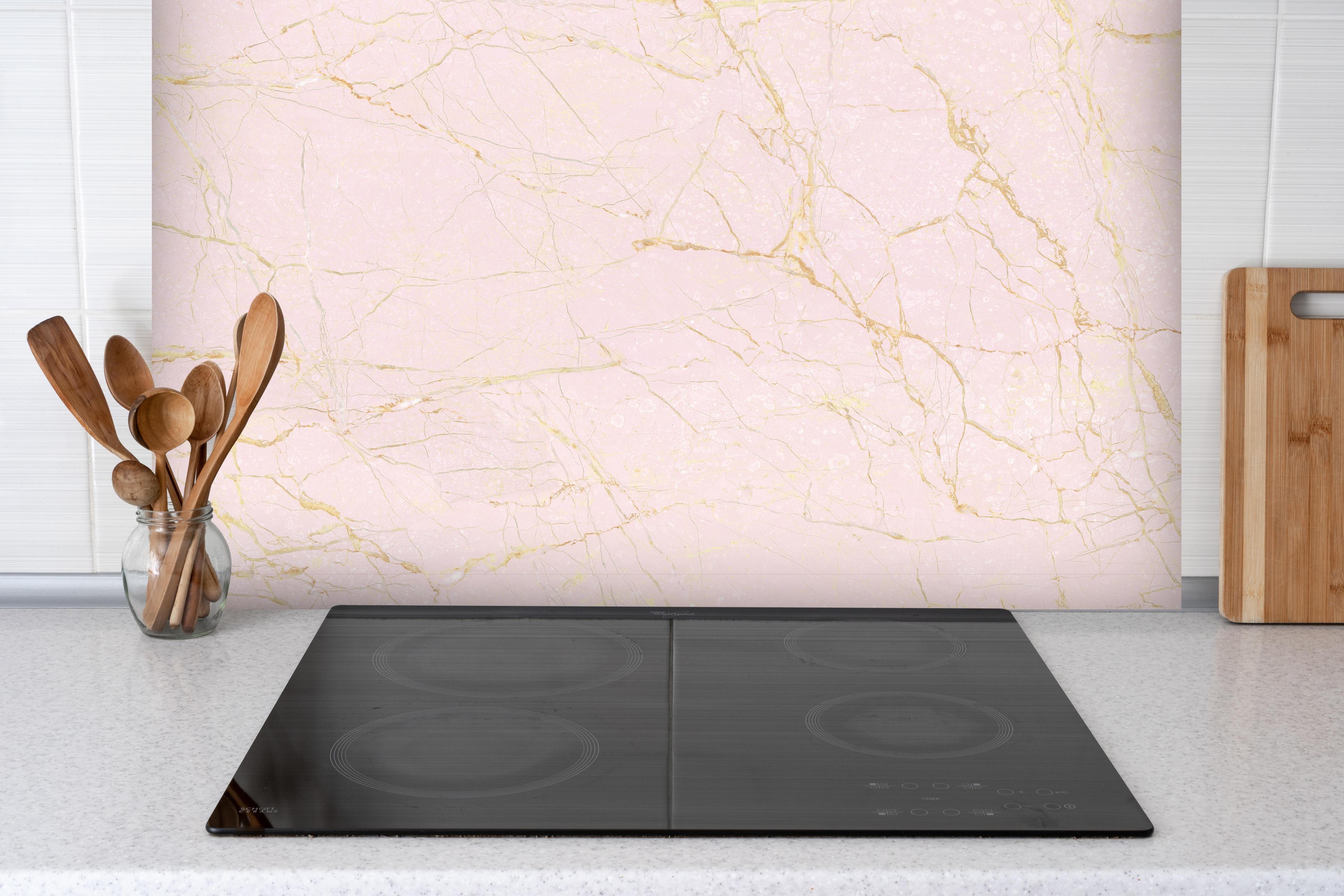 Spritzschutz - Rosa-Gold Marmor hinter einem Cerankochfeld zwischen Holz-Kochutensilien
