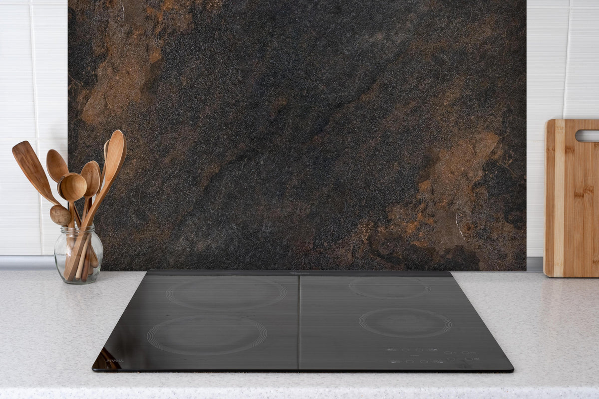 Spritzschutz - Schwarz braun rostigen Stein Fliesen  hinter einem Cerankochfeld zwischen Holz-Kochutensilien
