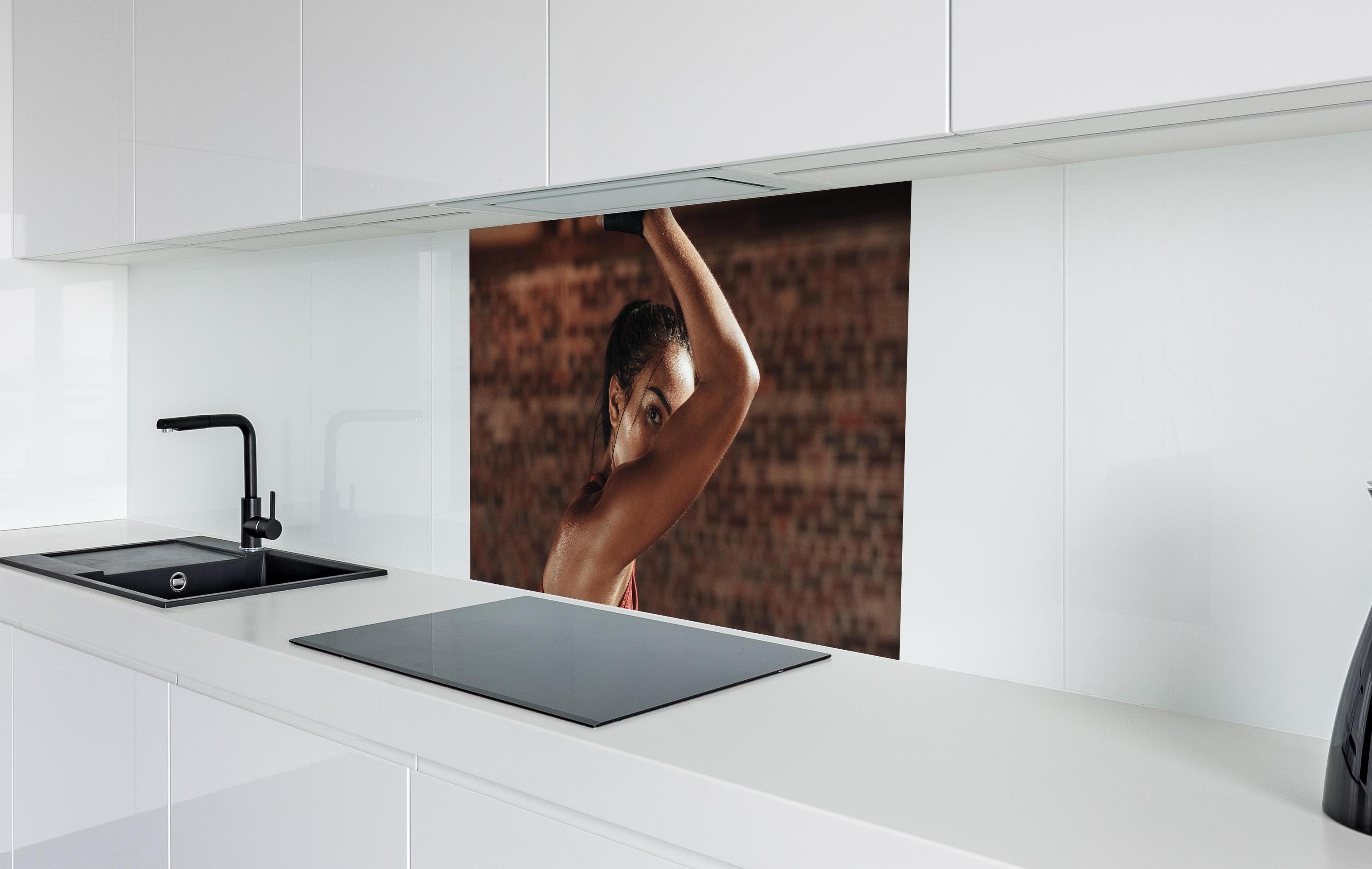 Spritzschutz - Starke Frau beim Training mit Dip-Ringen  in weißer Hochglanz-Küche hinter einem Cerankochfeld