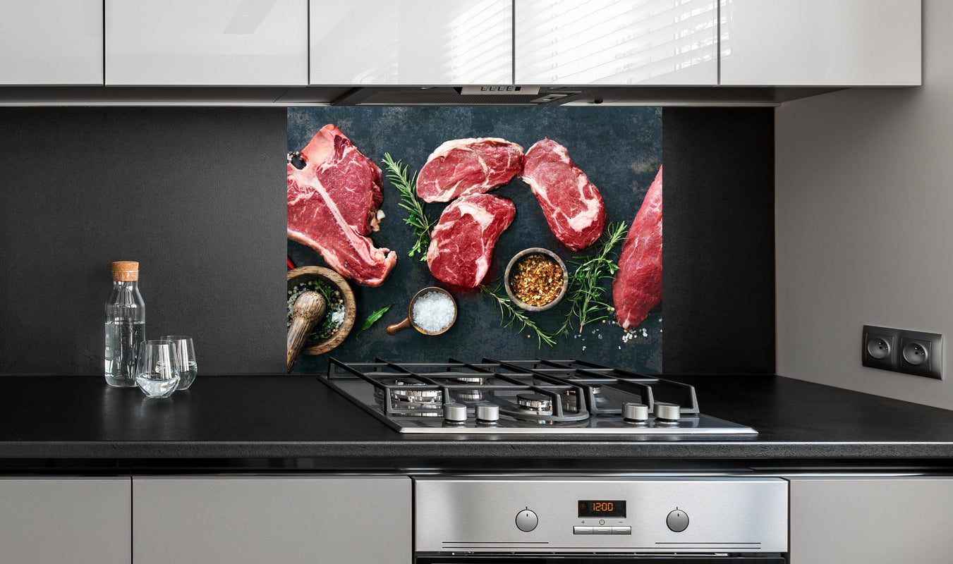 Spritzschutz - Steakvariationen auf Schieferplatte an edler Anthrazit-Wand hinter silbernem Gasherd