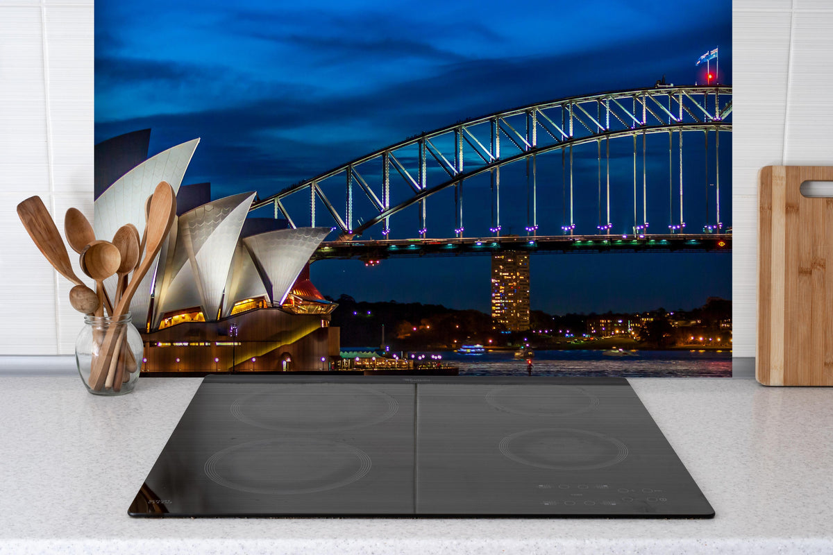 Spritzschutz - Sydney Harbour Bridge bei Nacht hinter einem Cerankochfeld zwischen Holz-Kochutensilien
