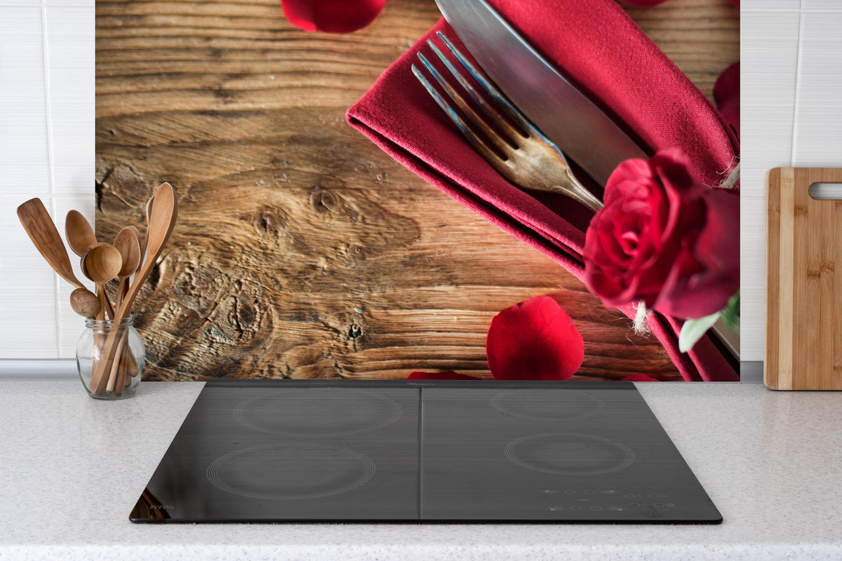 Spritzschutz - Tischdekoration mit roten Rosen hinter einem Cerankochfeld zwischen Holz-Kochutensilien
