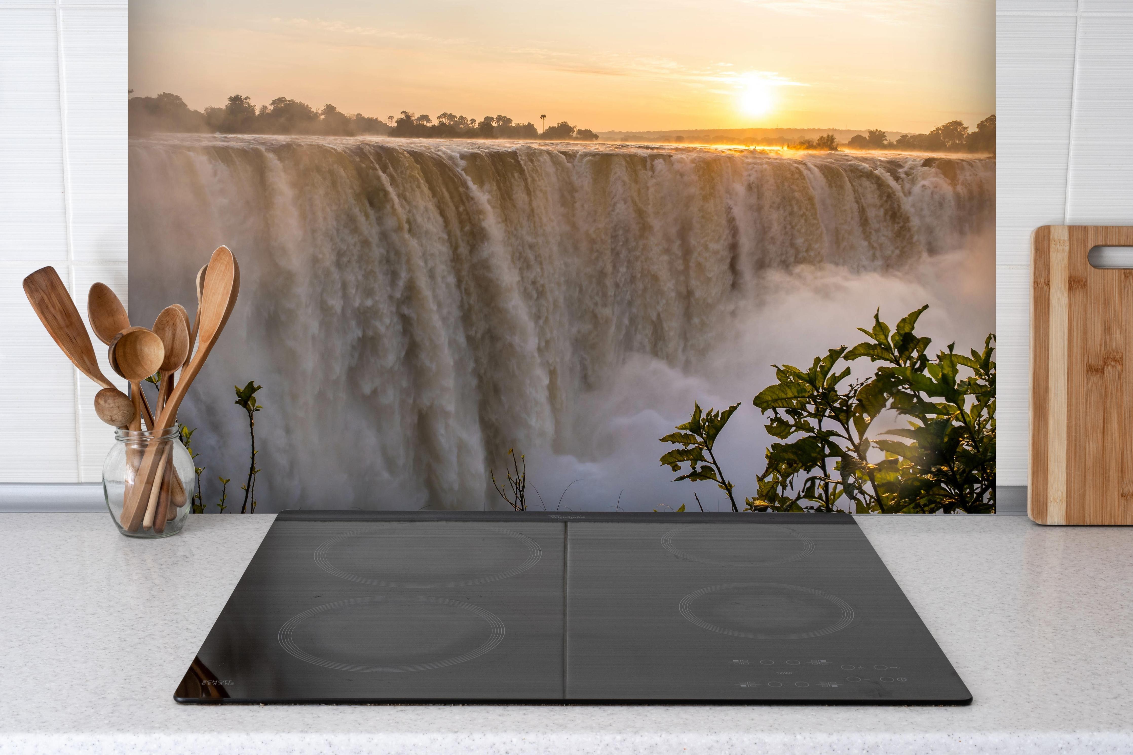 Spritzschutz - Victoriafälle bei Sonnenaufgang hinter einem Cerankochfeld zwischen Holz-Kochutensilien
