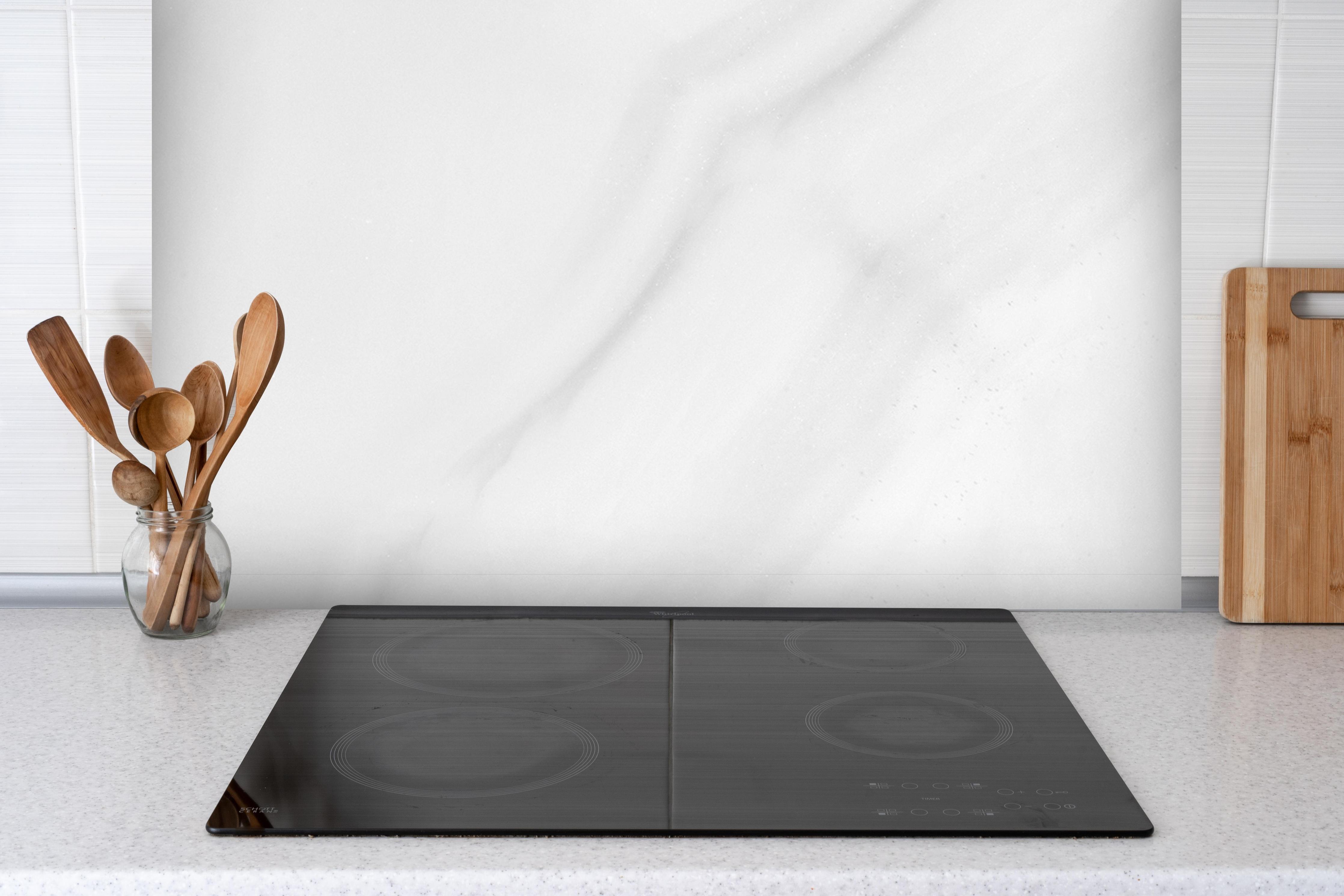 Spritzschutz - Weißer polierter Marmor hinter einem Cerankochfeld zwischen Holz-Kochutensilien
