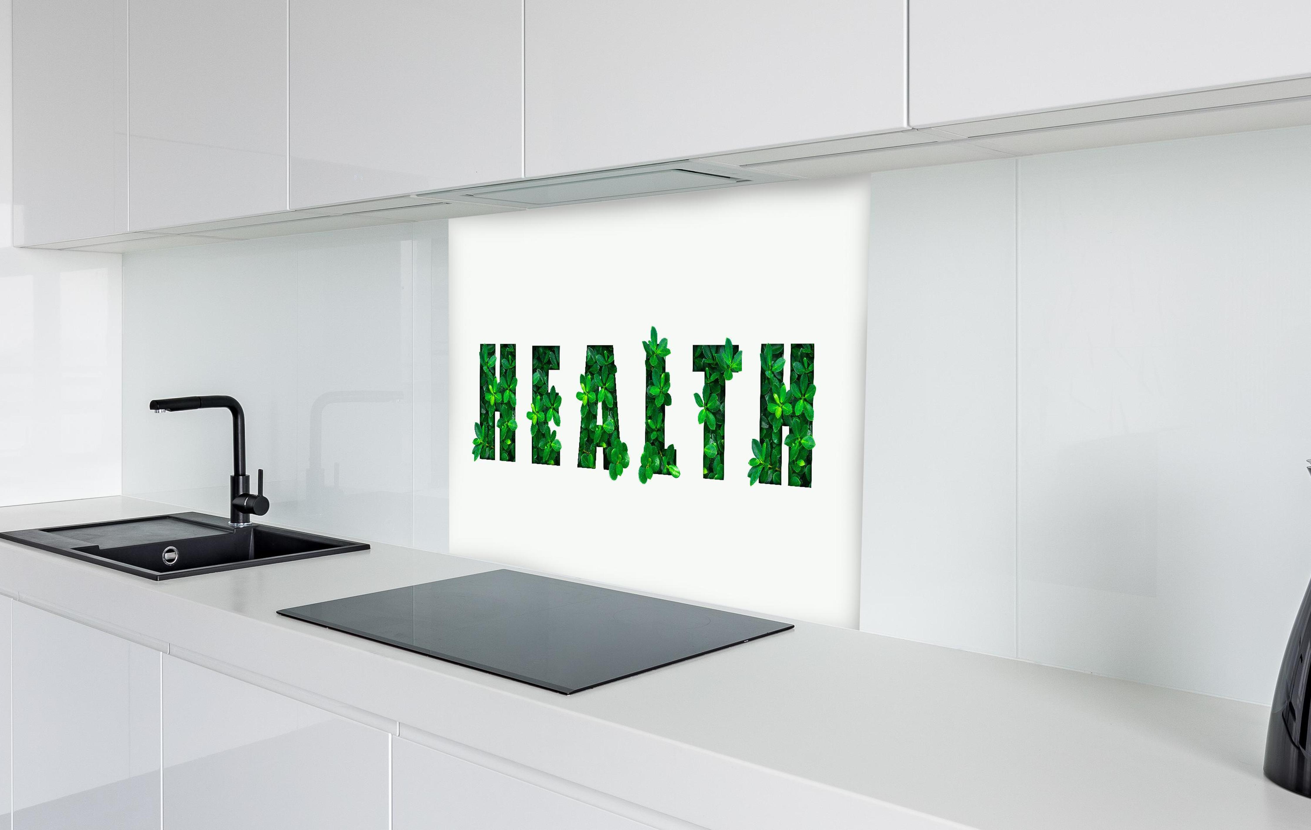 Spritzschutz - Wort HEALTH aus grünen Blättern  in weißer Hochglanz-Küche hinter einem Cerankochfeld