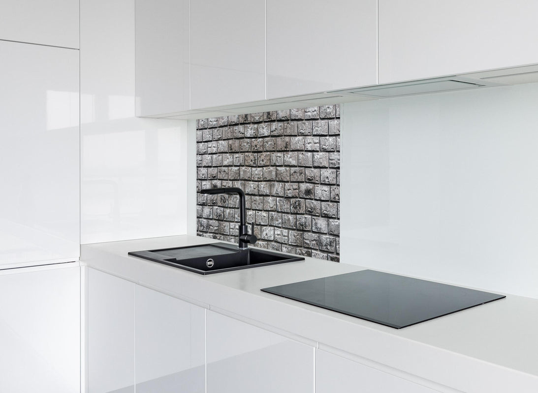 Spritzschutz - Ziegelmauer aus dekorativem grauem Stein hinter modernem schwarz-matten Spülbecken in weißer Hochglanz-Küche