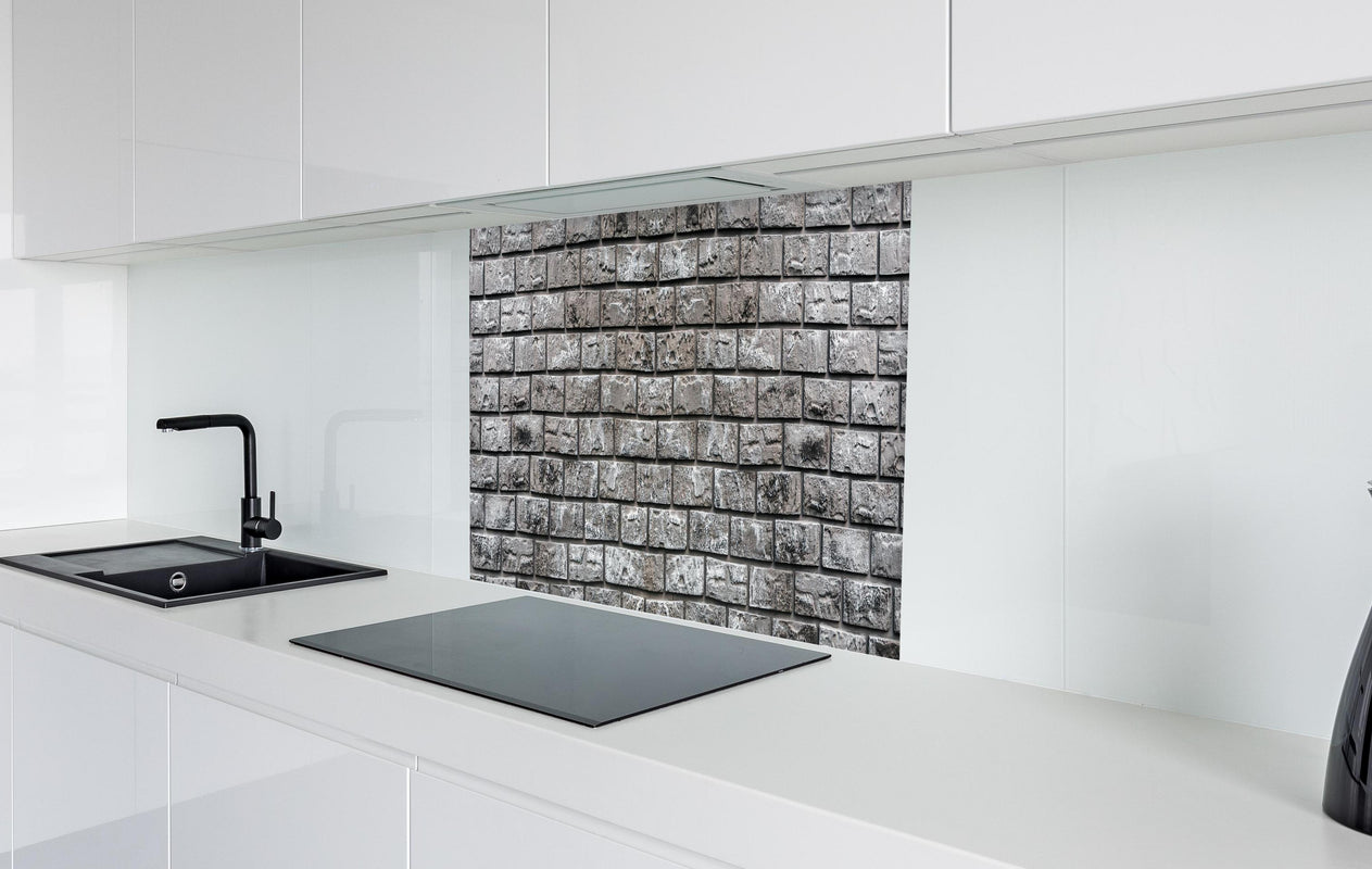Spritzschutz - Ziegelmauer aus dekorativem grauem Stein  in weißer Hochglanz-Küche hinter einem Cerankochfeld