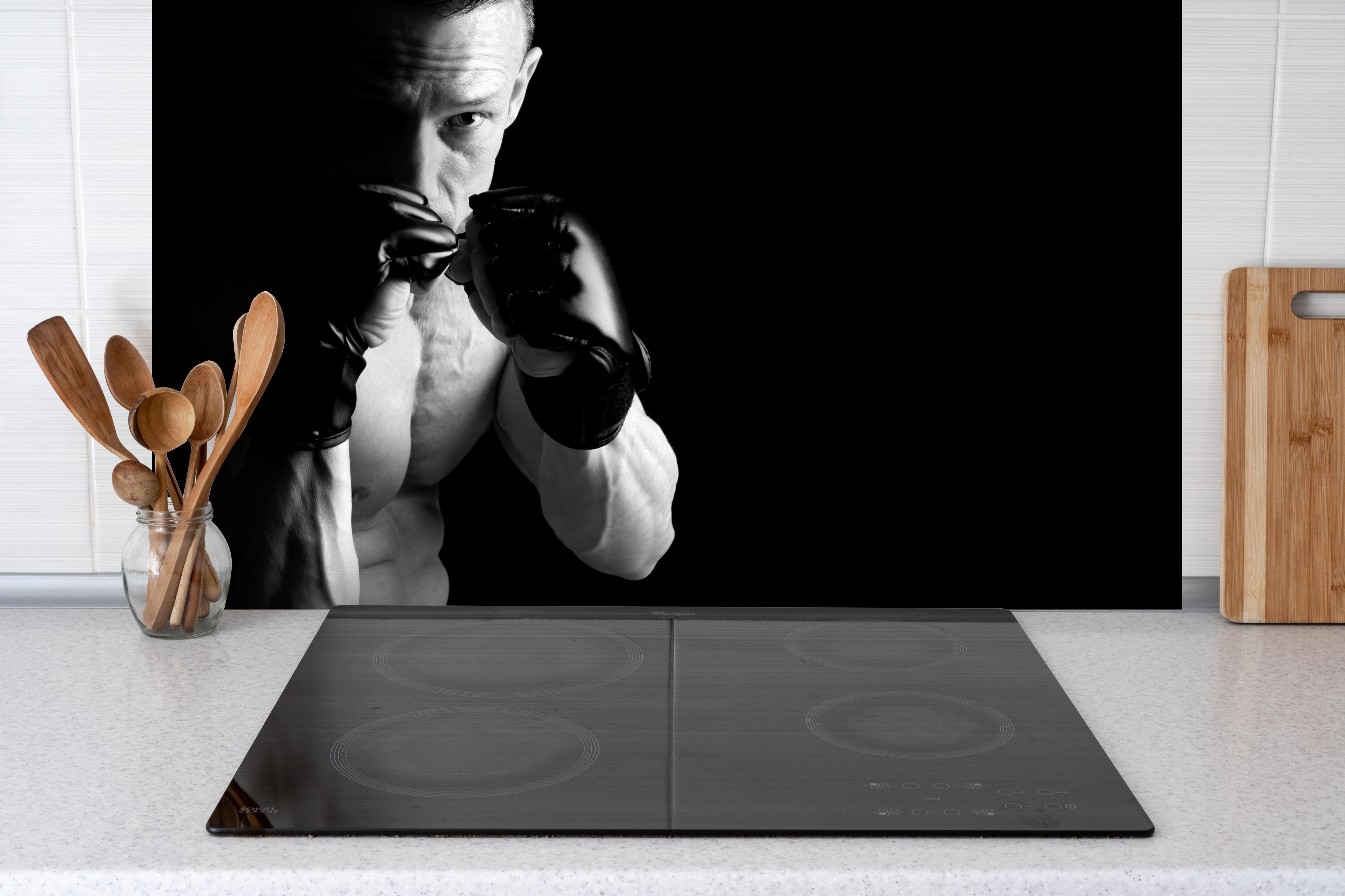 Spritzschutz - athletischer MMA-Sportler hinter einem Cerankochfeld zwischen Holz-Kochutensilien
