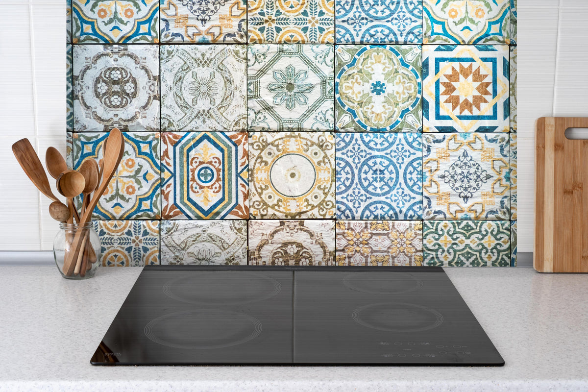 Spritzschutz - buntes Mosaik im spanischen Stil hinter einem Cerankochfeld zwischen Holz-Kochutensilien
