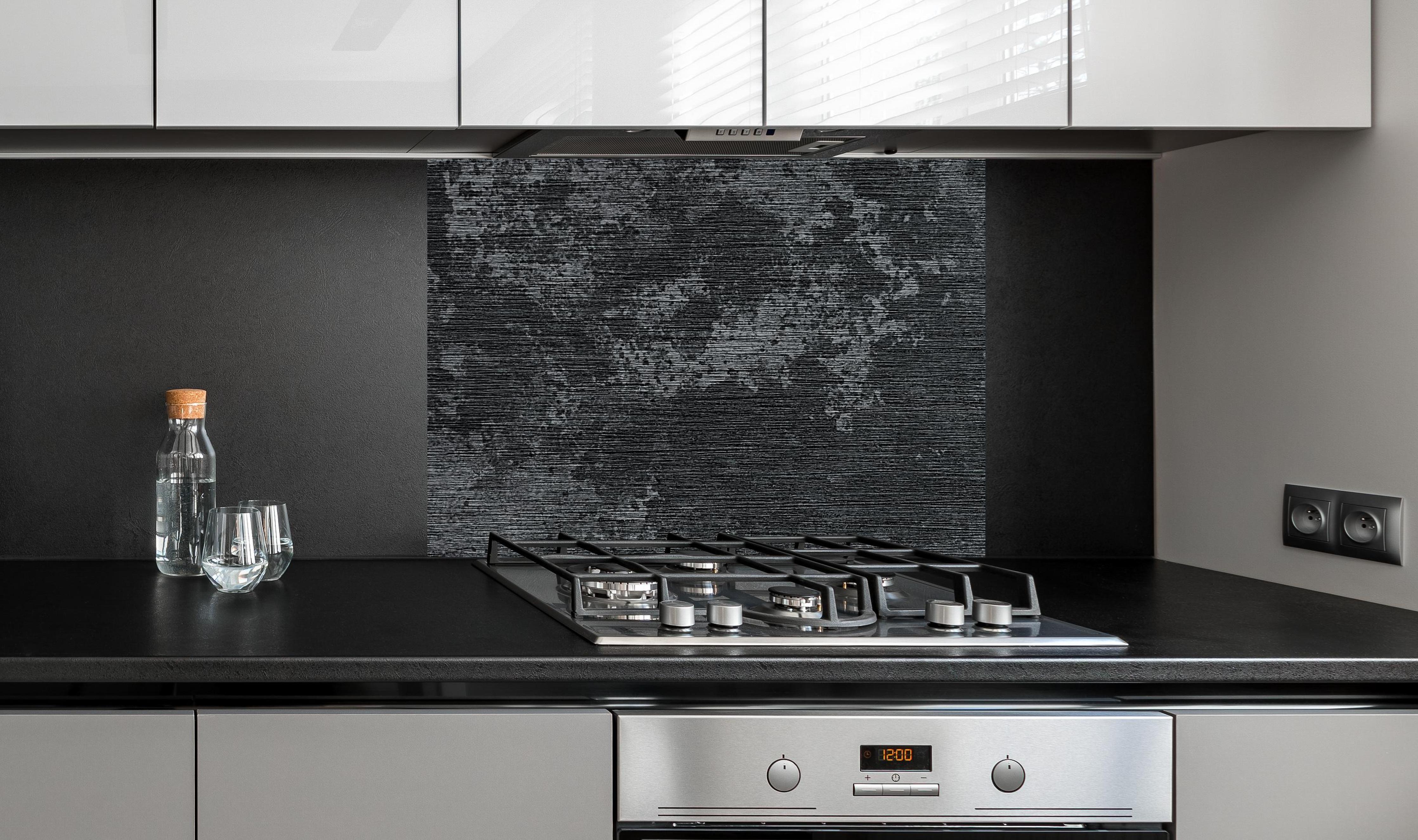 Spritzschutz - wild gebürstetes Metall an edler Anthrazit-Wand hinter silbernem Gasherd