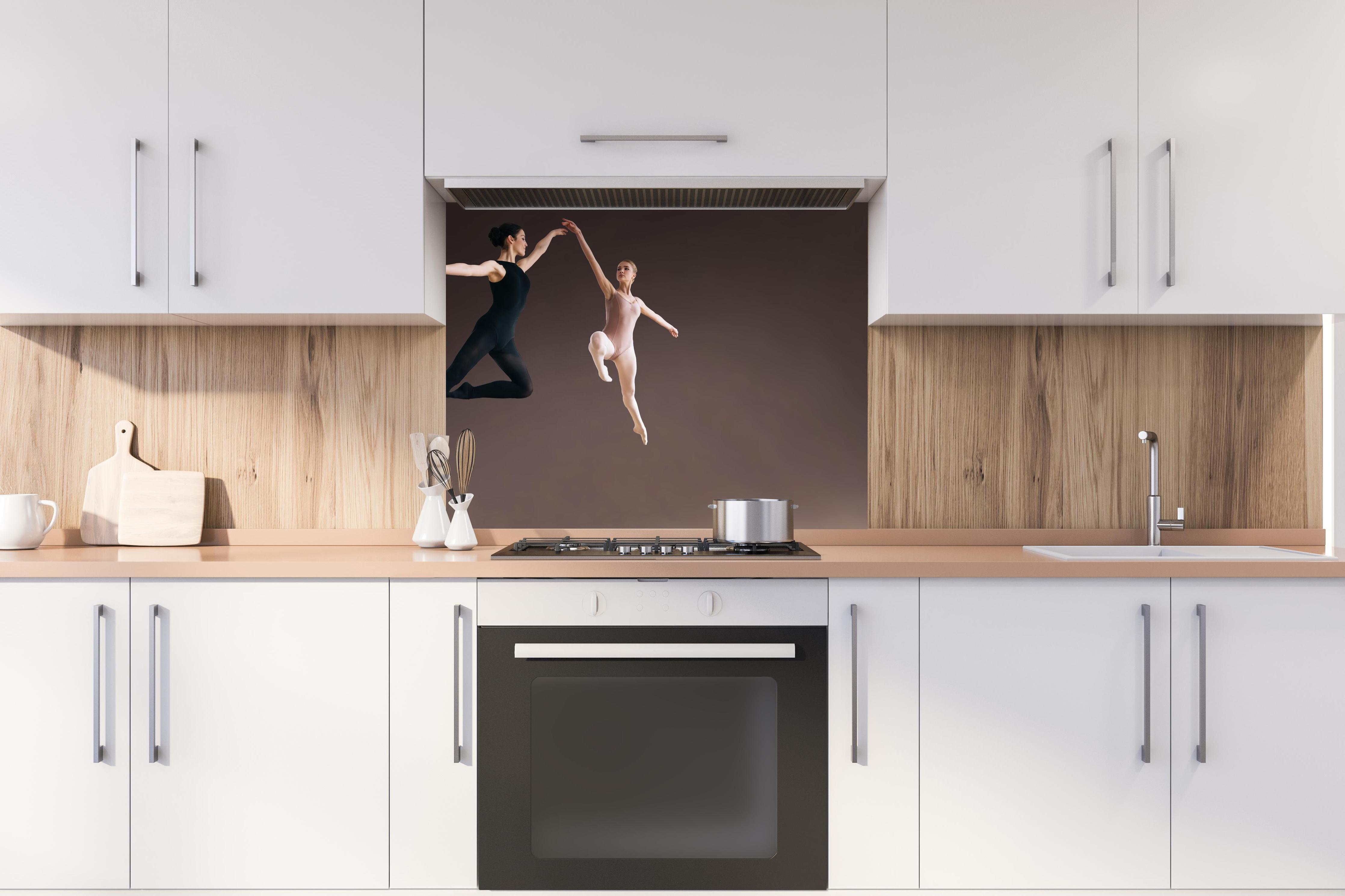 Spritzschutz - zwei Balletttänzerinnen hoch in der Luft hinter einem Cerankochfeld zwischen Holz-Kochutensilien
