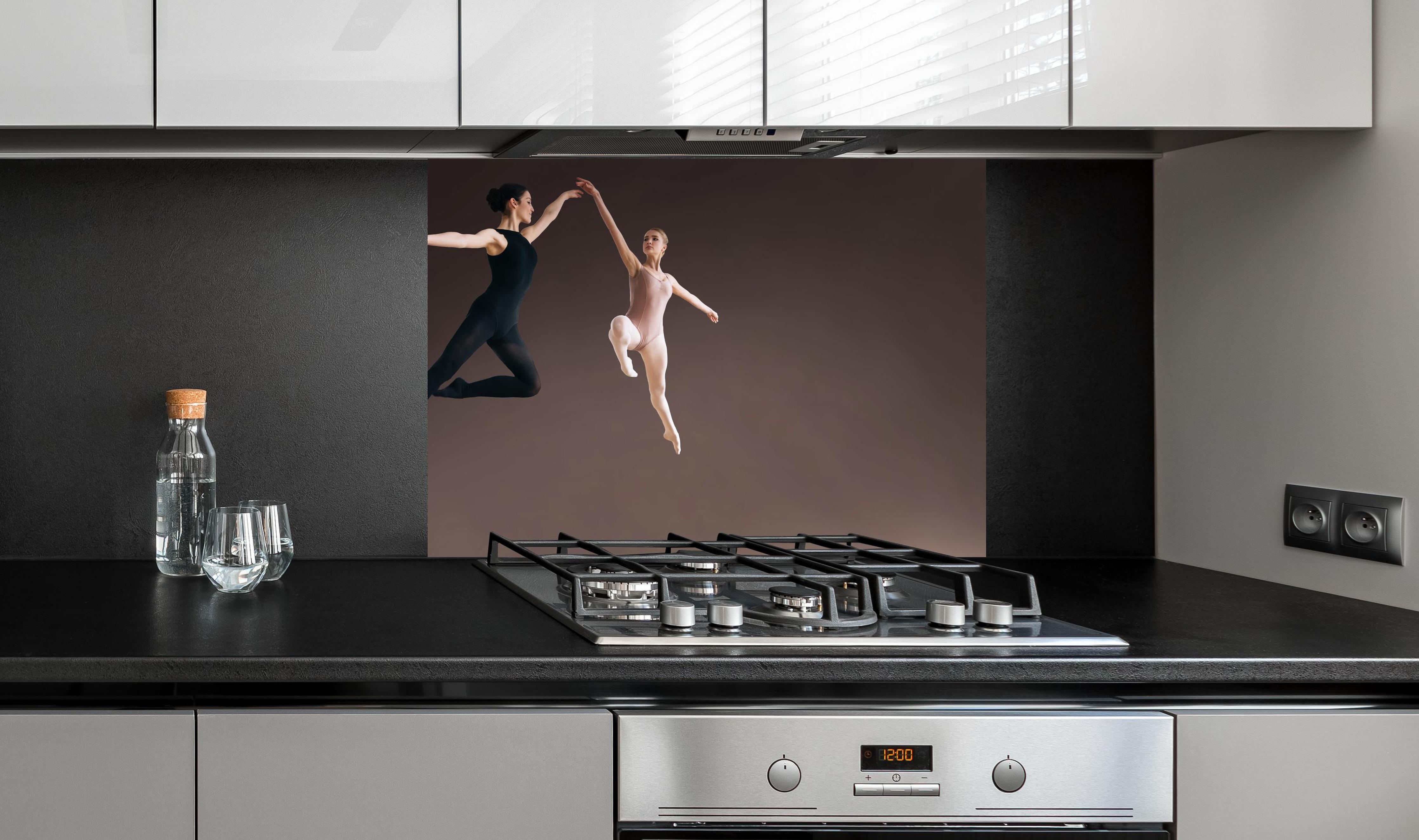 Spritzschutz - zwei Balletttänzerinnen hoch in der Luft hinter einem Cerankochfeld zwischen Holz-Kochutensilien
