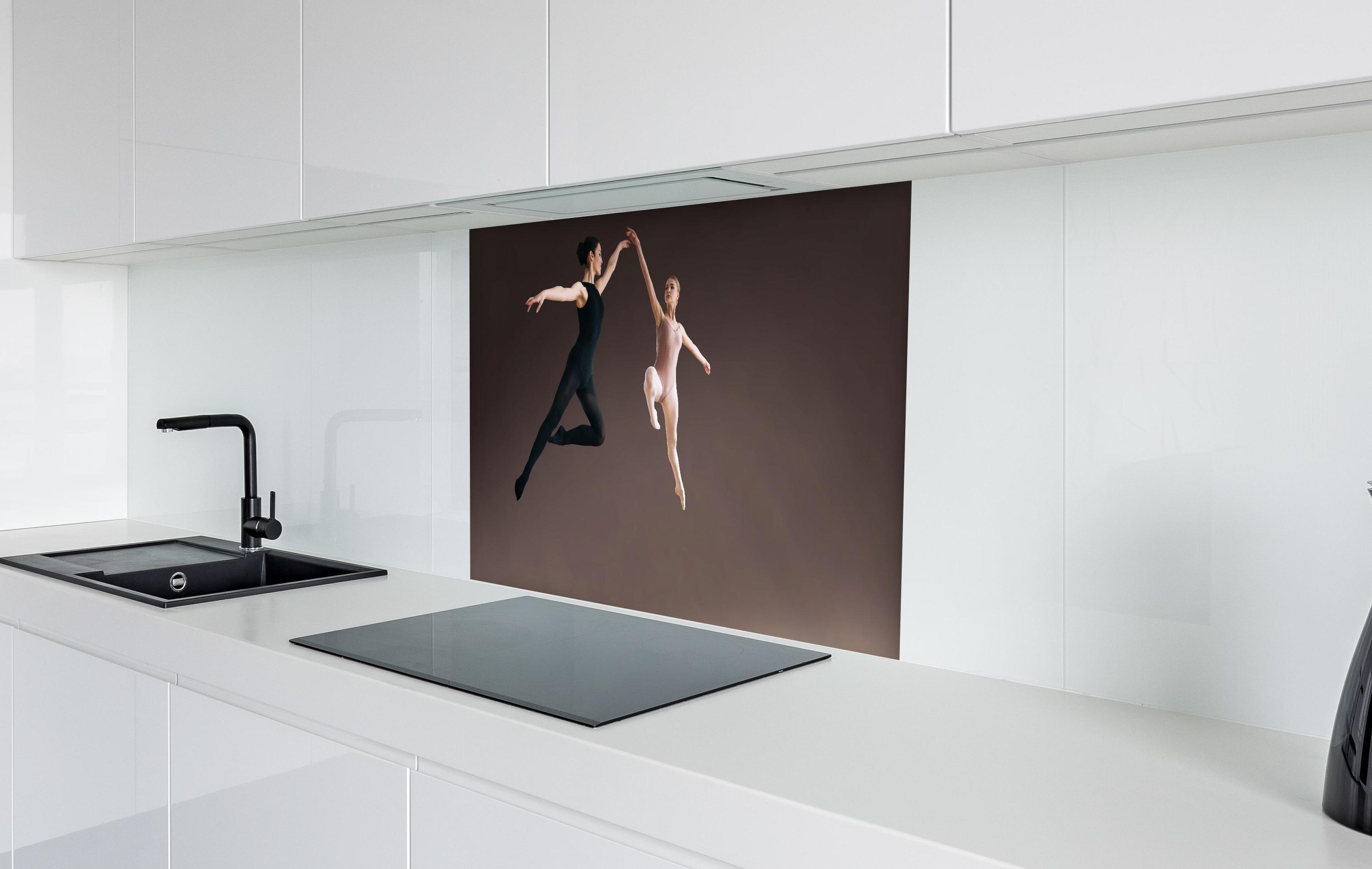 Spritzschutz - zwei Balletttänzerinnen hoch in der Luft hinter einem Cerankochfeld zwischen Holz-Kochutensilien
