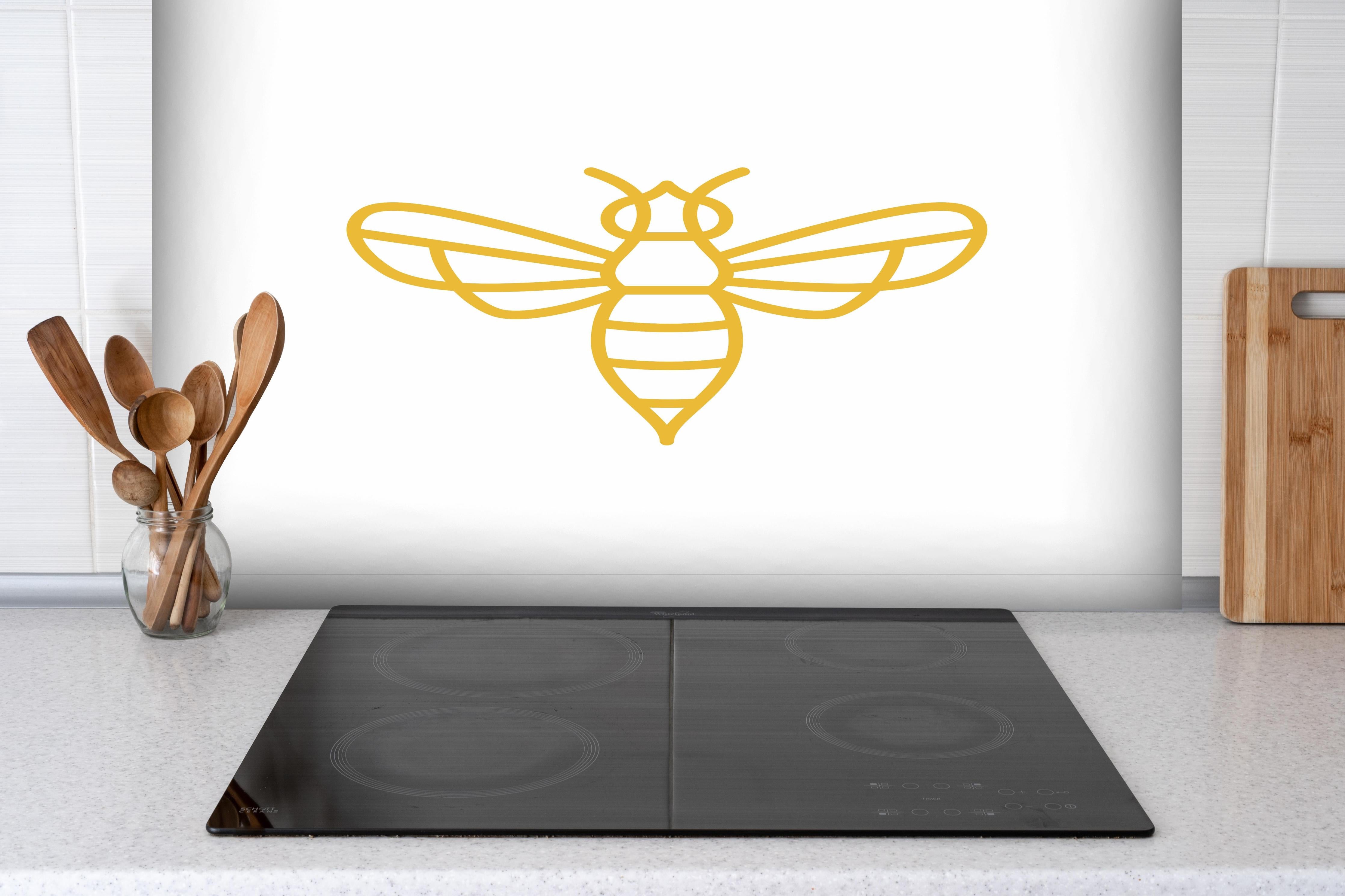 Spritzschutz - Stilisierte Goldfarbene Biene Illustration hinter einem Cerankochfeld zwischen Holz-Kochutensilien
