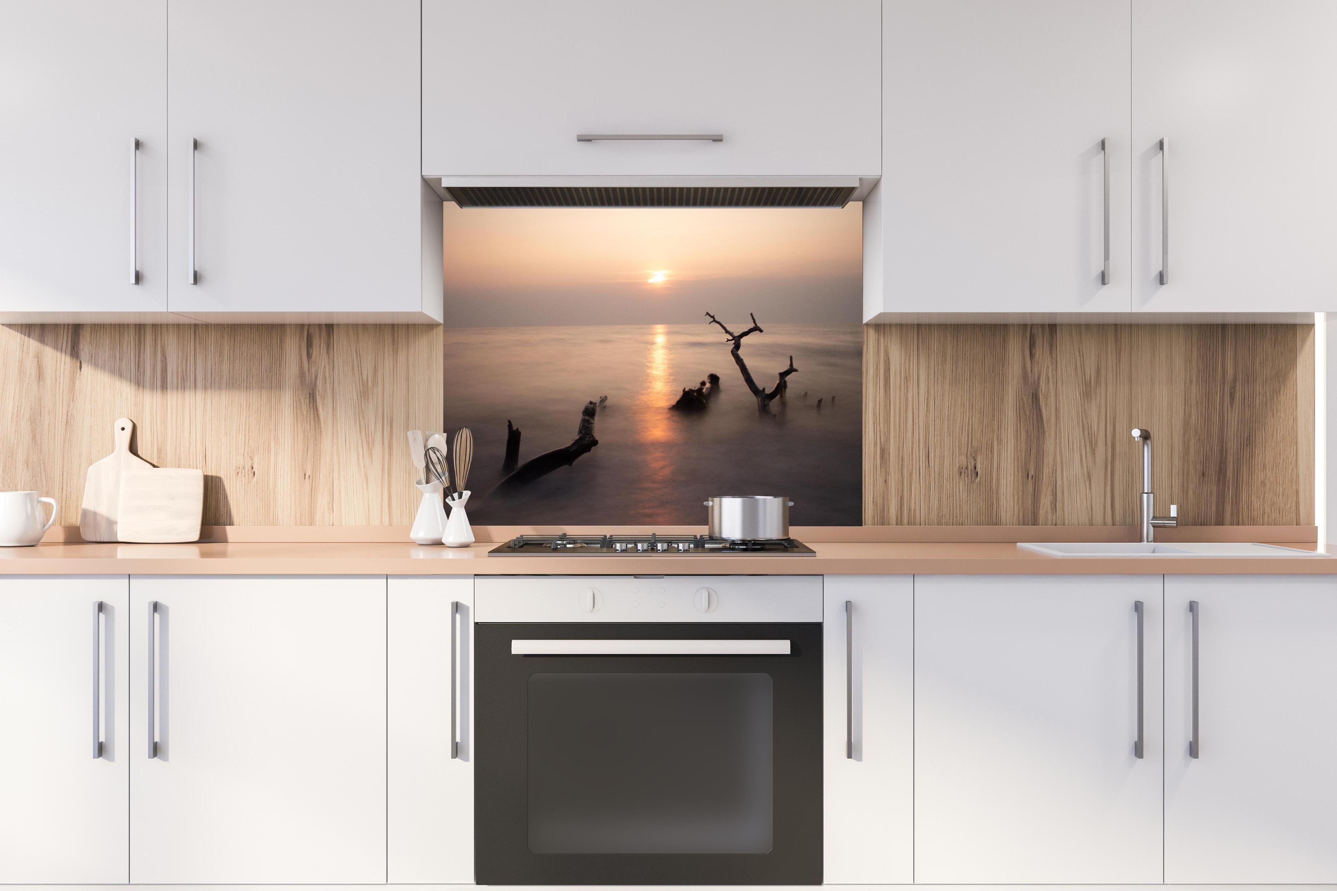 Spritzschutz - Stimmungsvoller Sonnenuntergangs-Strand hinter einem Cerankochfeld zwischen Holz-Kochutensilien
