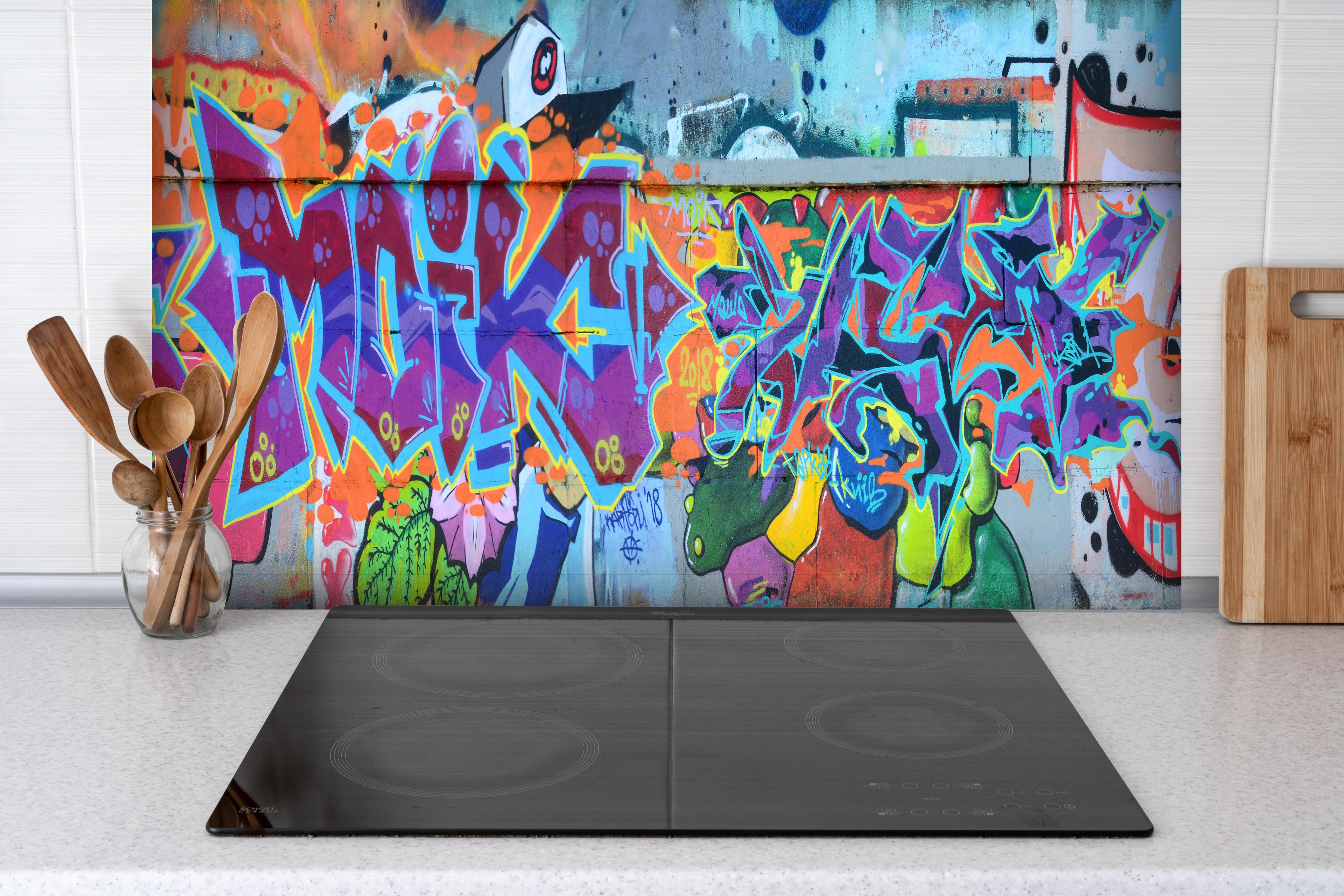 Spritzschutz - Street Art Graffiti in Lila-Tönen hinter einem Cerankochfeld zwischen Holz-Kochutensilien
