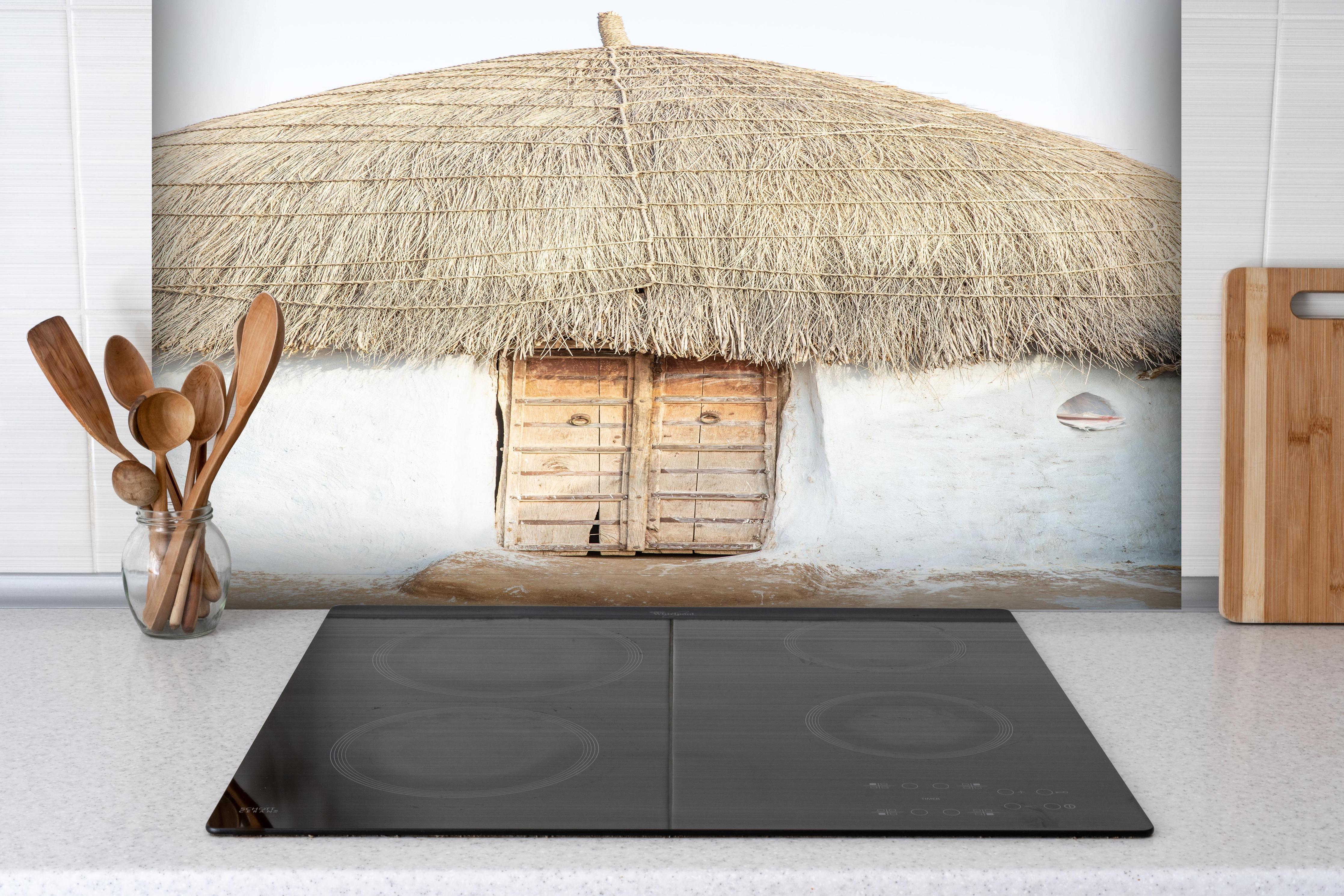Spritzschutz - Traditionelle Wüstenhütte mit Strohdach hinter einem Cerankochfeld zwischen Holz-Kochutensilien
