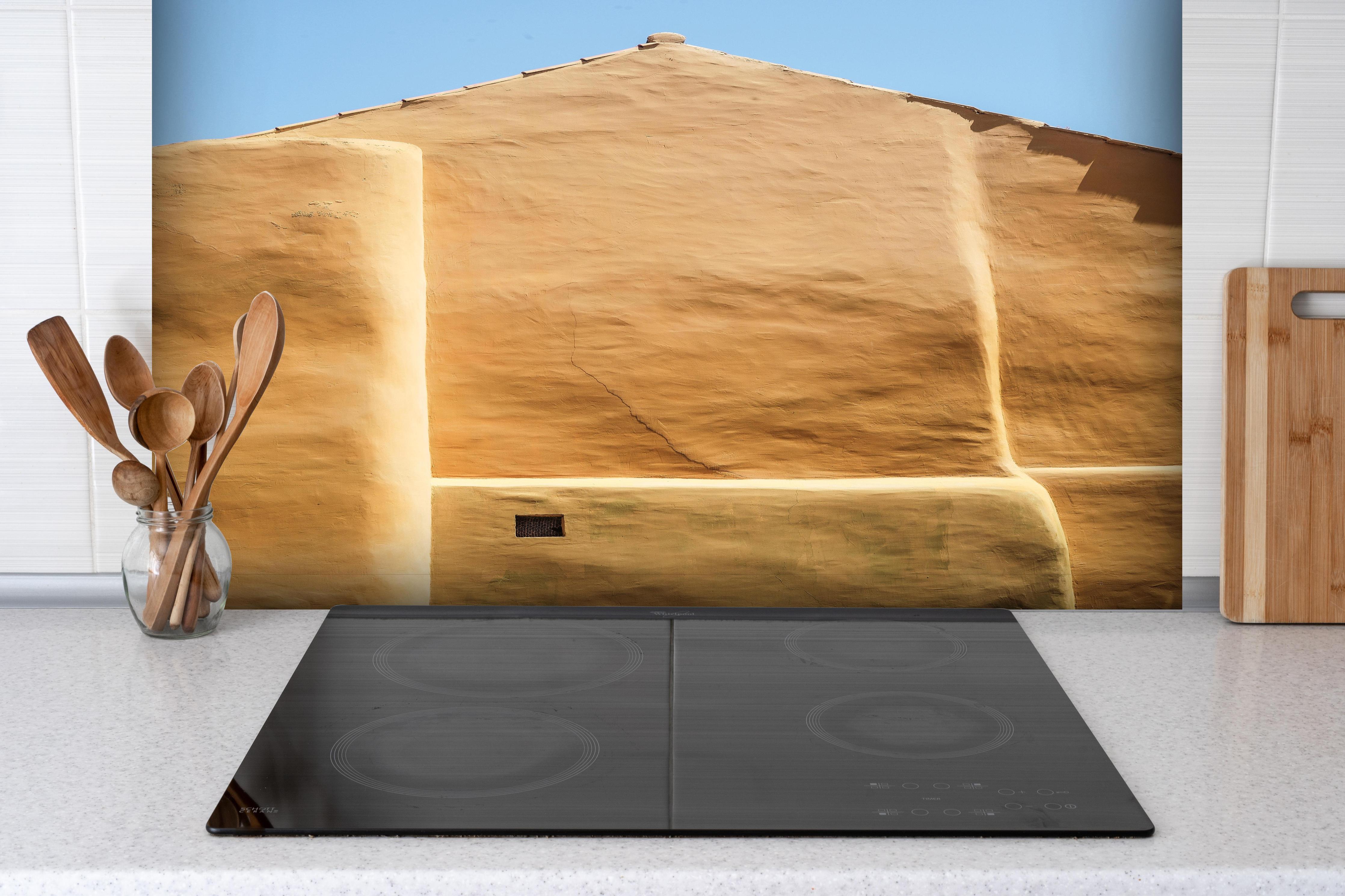 Spritzschutz - Traditionelle beigefarbene Lehmarchitektur hinter einem Cerankochfeld zwischen Holz-Kochutensilien
