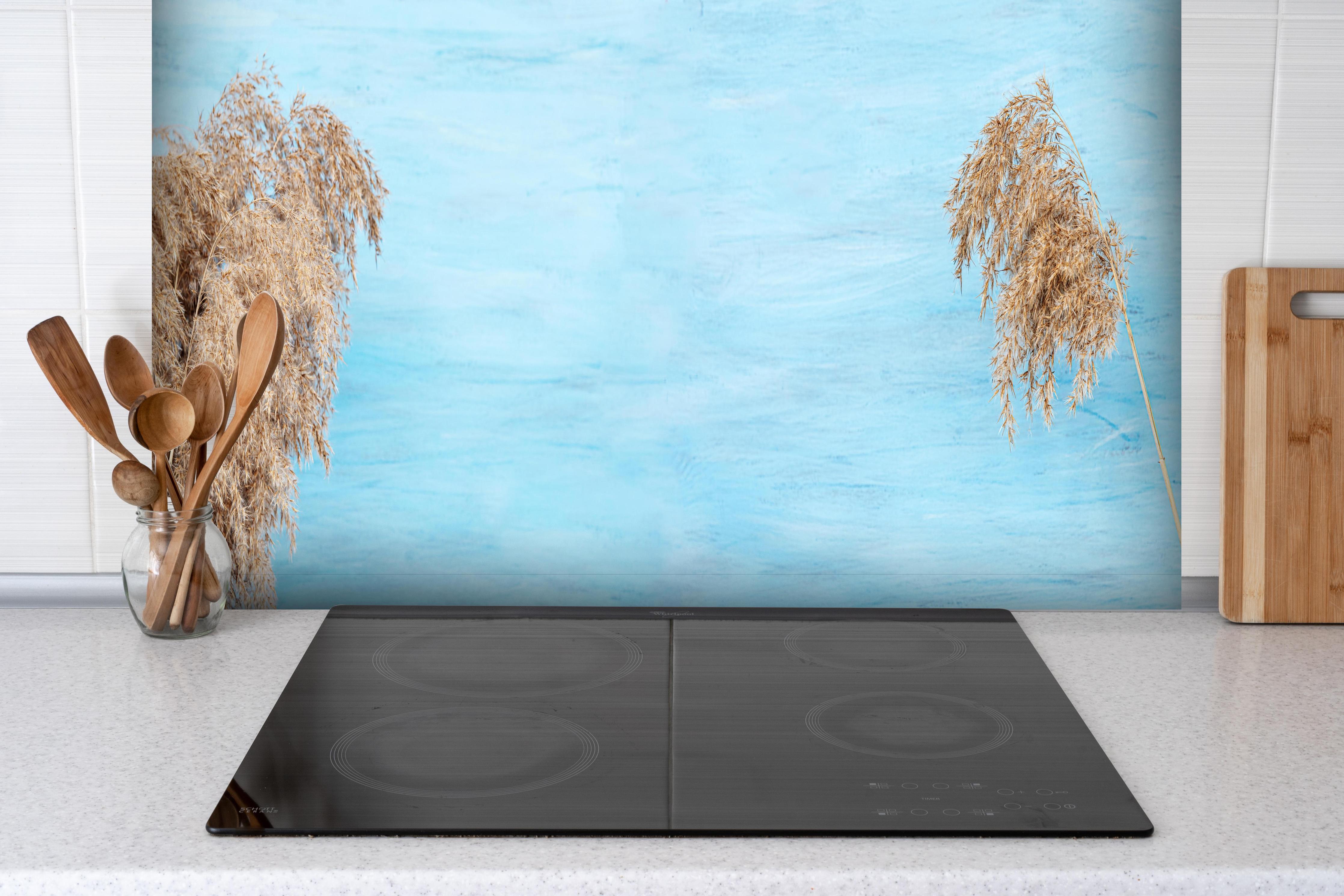 Spritzschutz - Trockene Pflanzen über dem Meer hinter einem Cerankochfeld zwischen Holz-Kochutensilien
