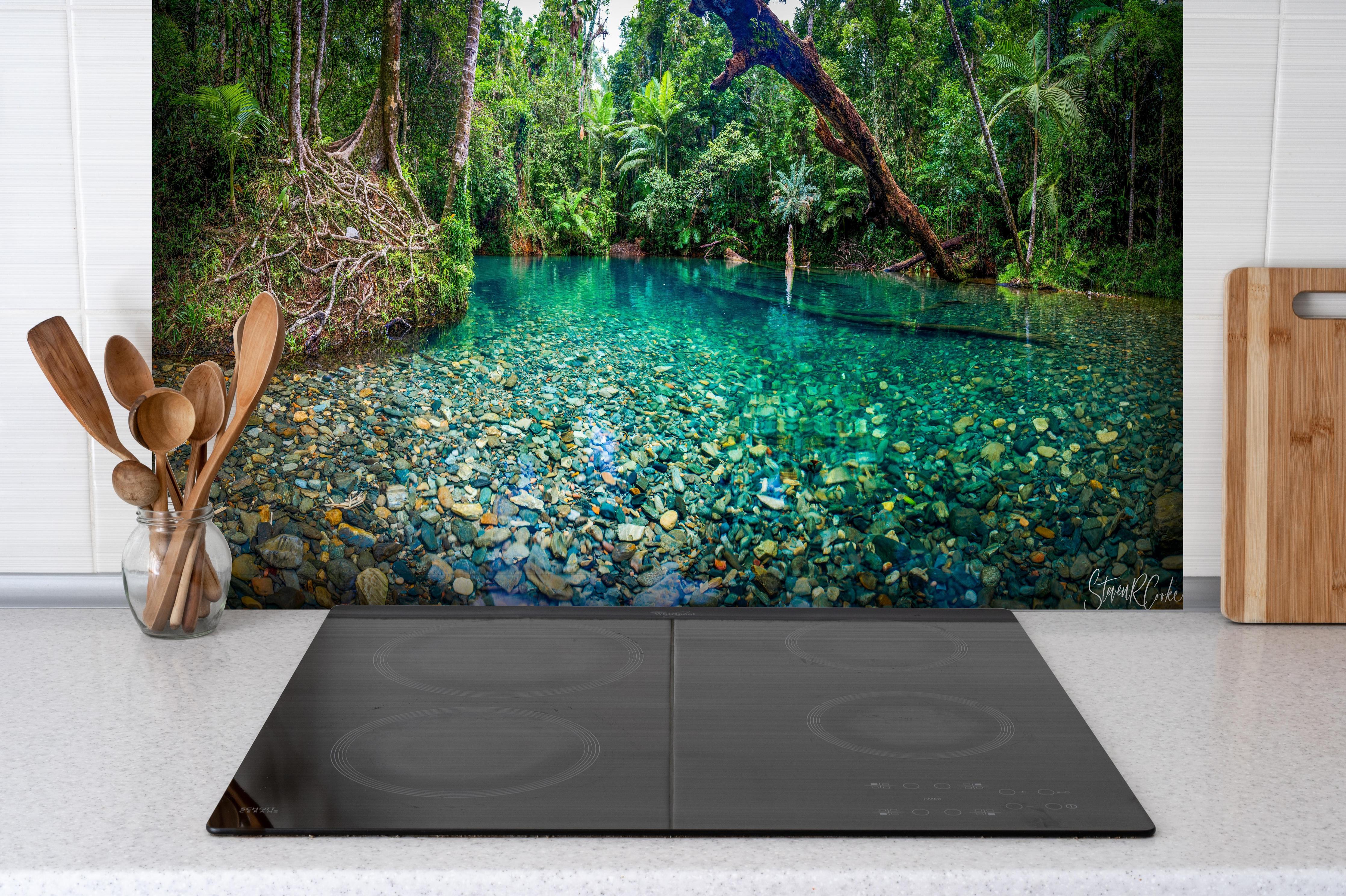 Spritzschutz - Tropischer Bach mit klarem Wasser hinter einem Cerankochfeld zwischen Holz-Kochutensilien
