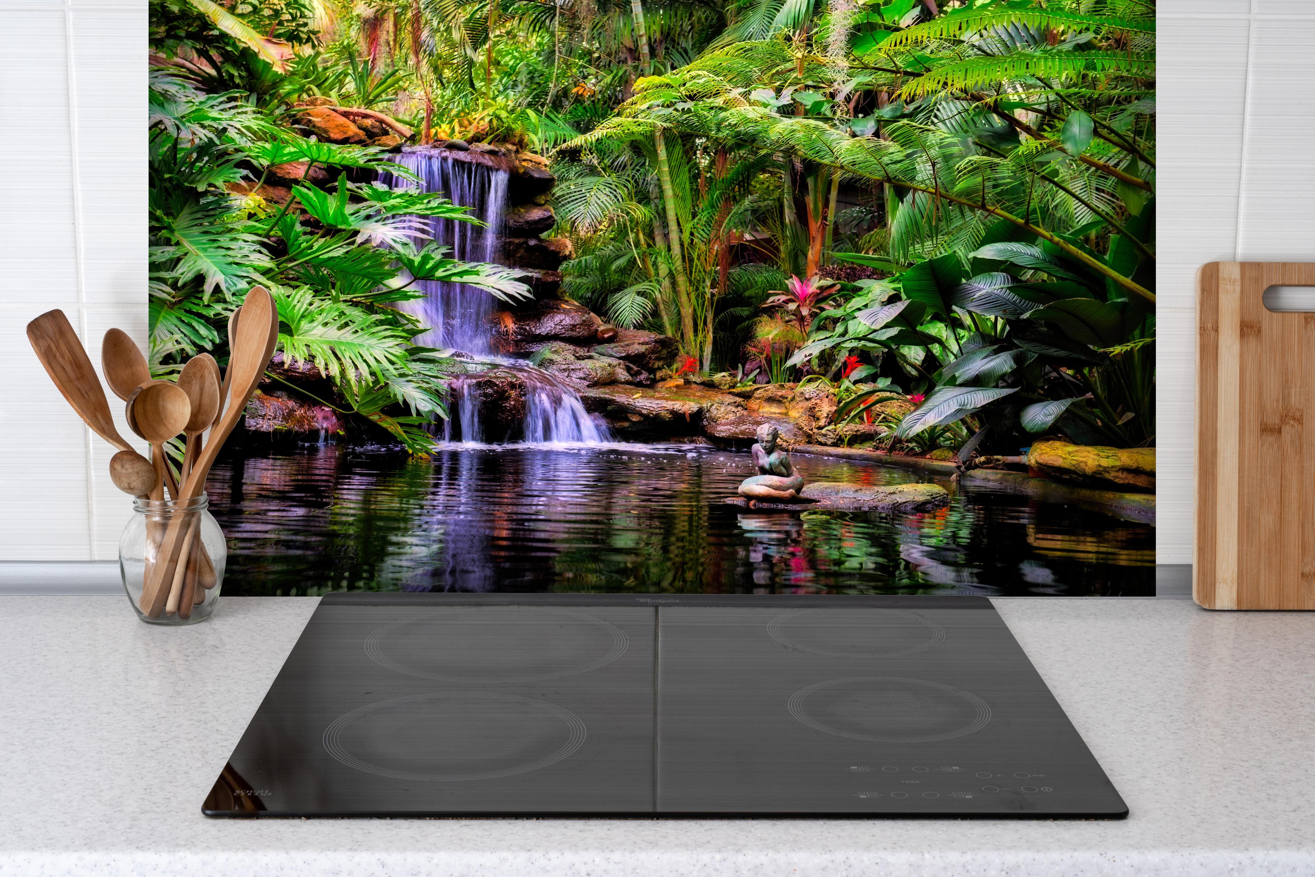 Spritzschutz - Tropischer Wasserfall hinter einem Cerankochfeld zwischen Holz-Kochutensilien
