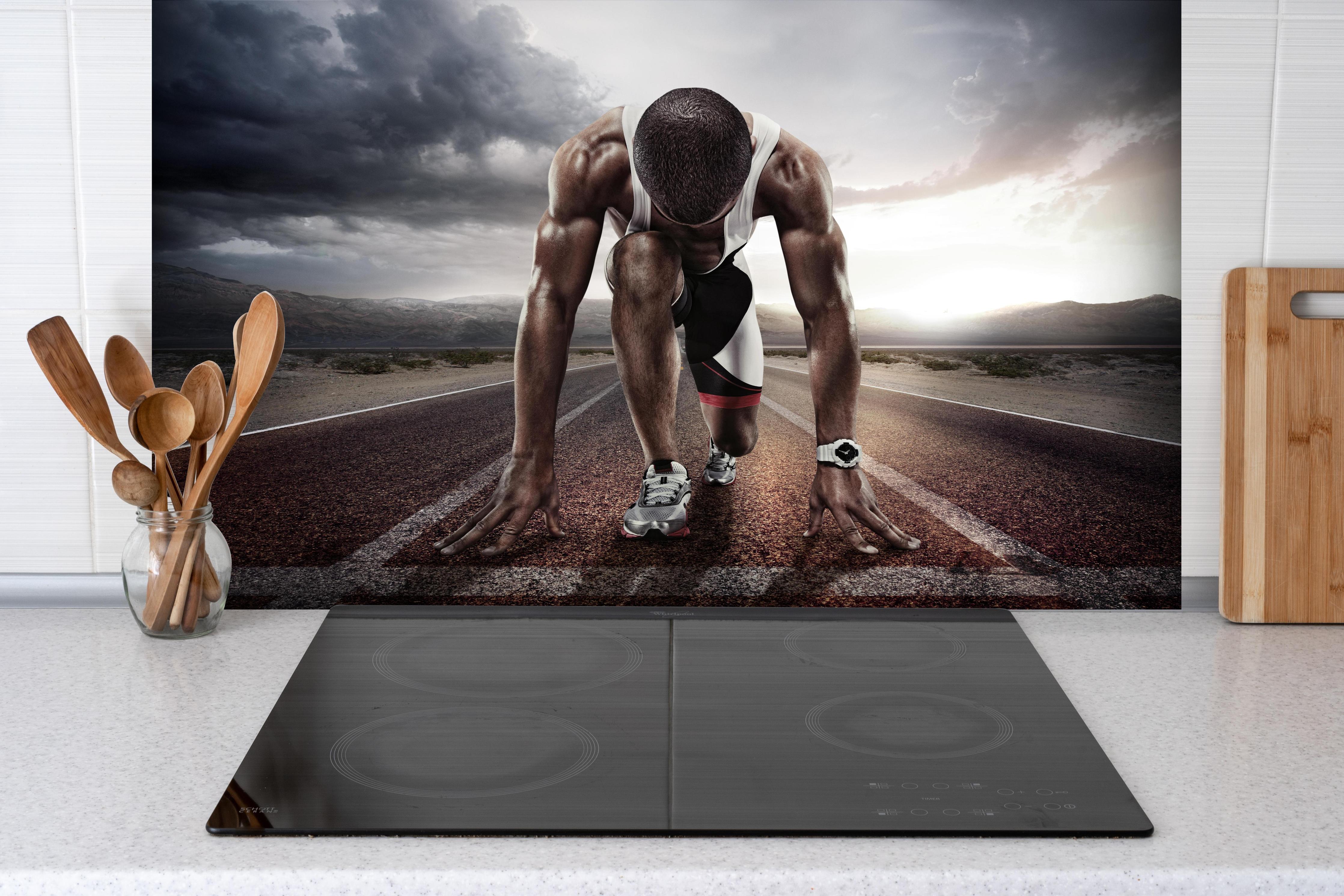 Spritzschutz - Ungewöhnliche Laufstrecke - Athlet hinter einem Cerankochfeld zwischen Holz-Kochutensilien
