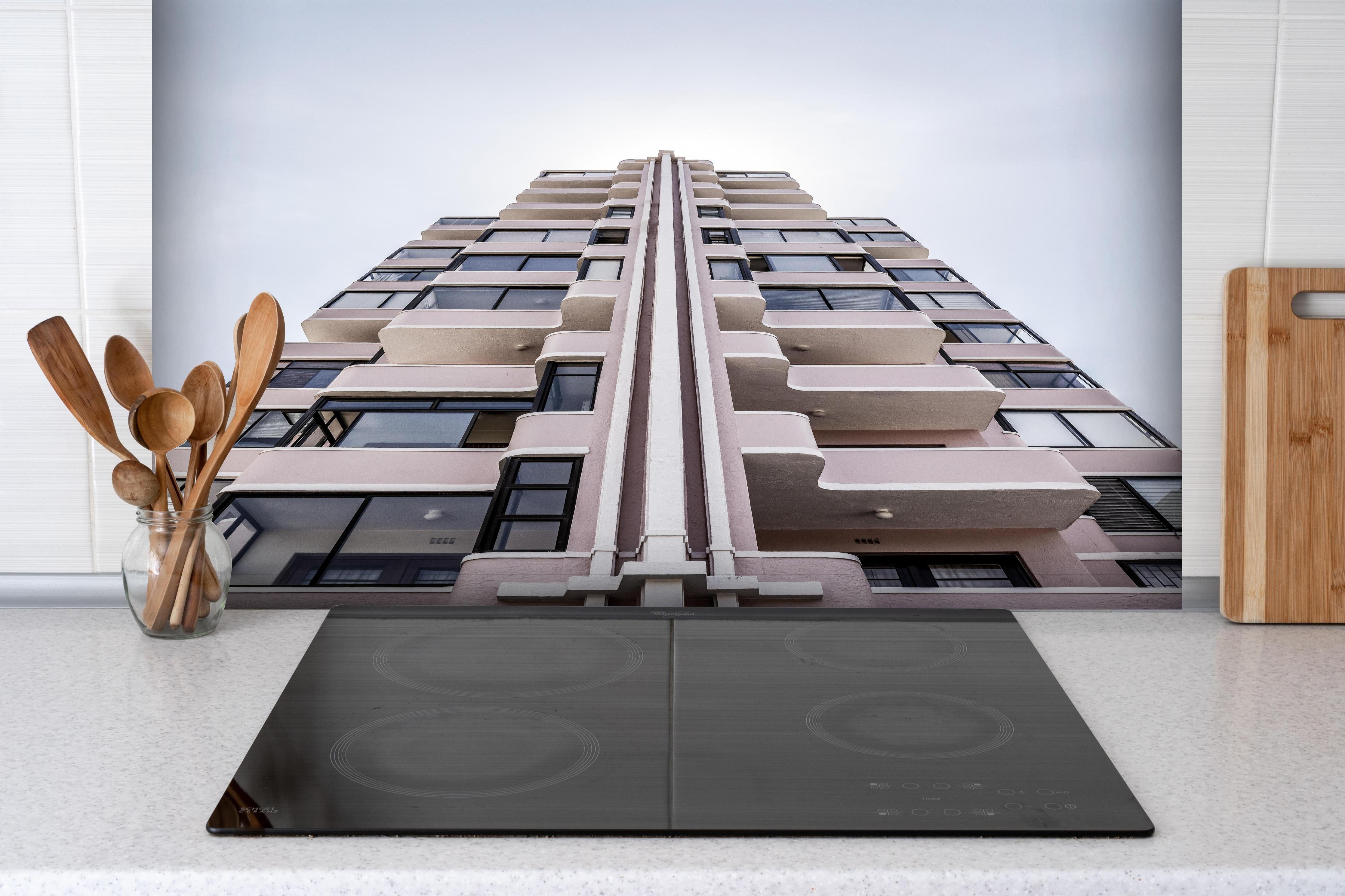 Spritzschutz - Urbanes Hochhaus mit grau-beigen Akzenten hinter einem Cerankochfeld zwischen Holz-Kochutensilien
