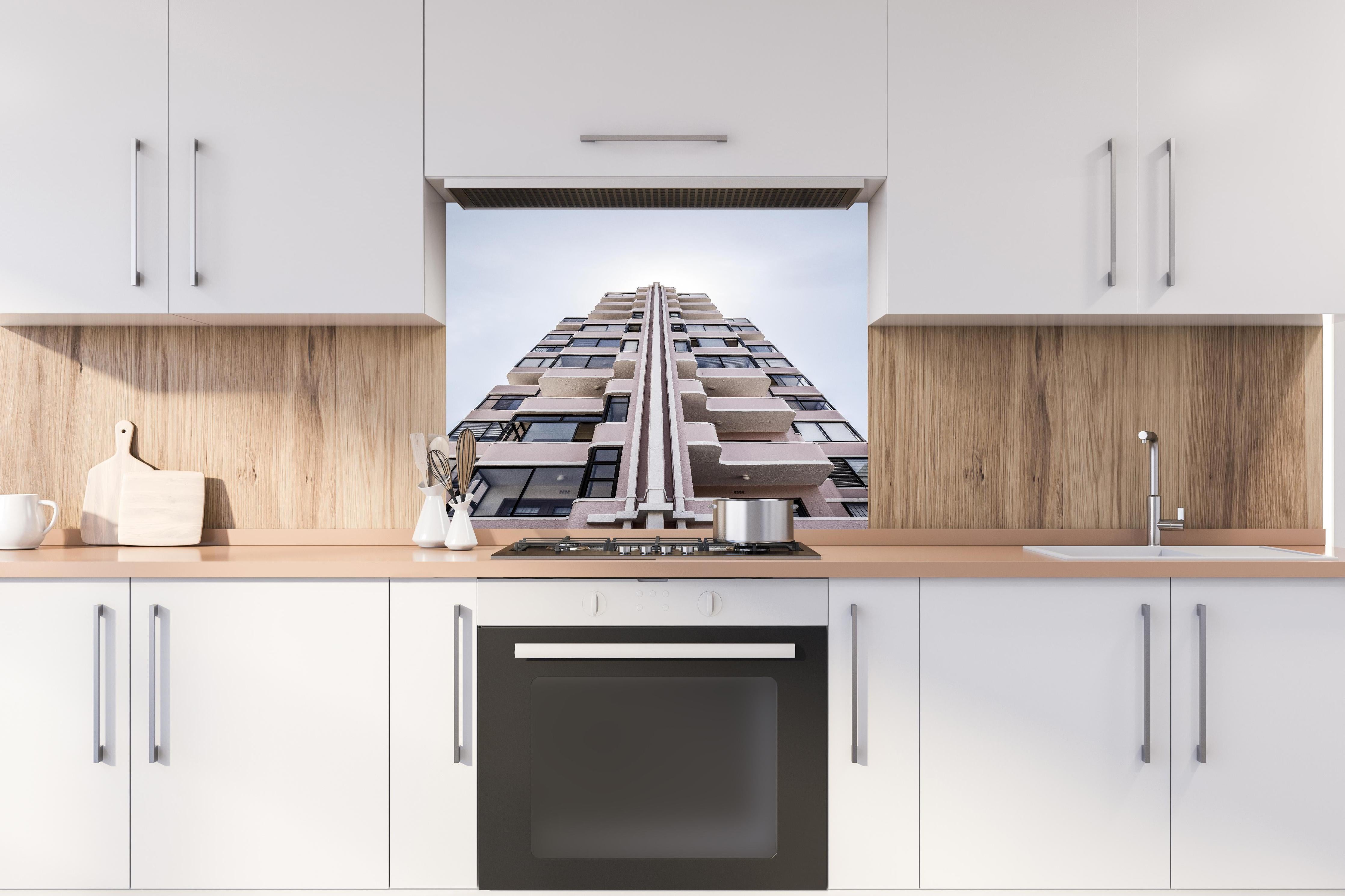 Spritzschutz - Urbanes Hochhaus mit grau-beigen Akzenten hinter einem Cerankochfeld zwischen Holz-Kochutensilien
