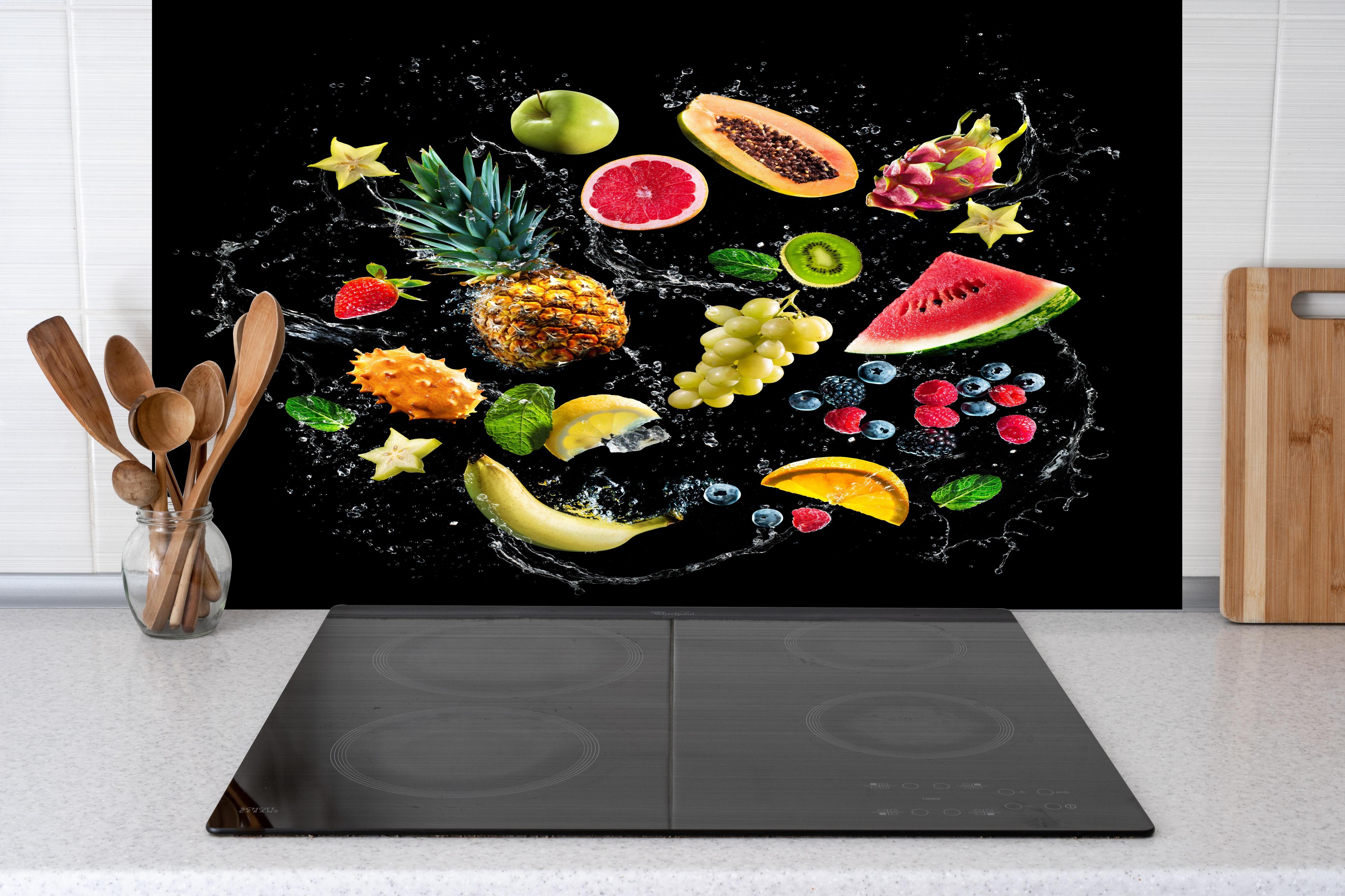 Spritzschutz - Verschiedenste Früchte mit Wasserspritzern hinter einem Cerankochfeld zwischen Holz-Kochutensilien
