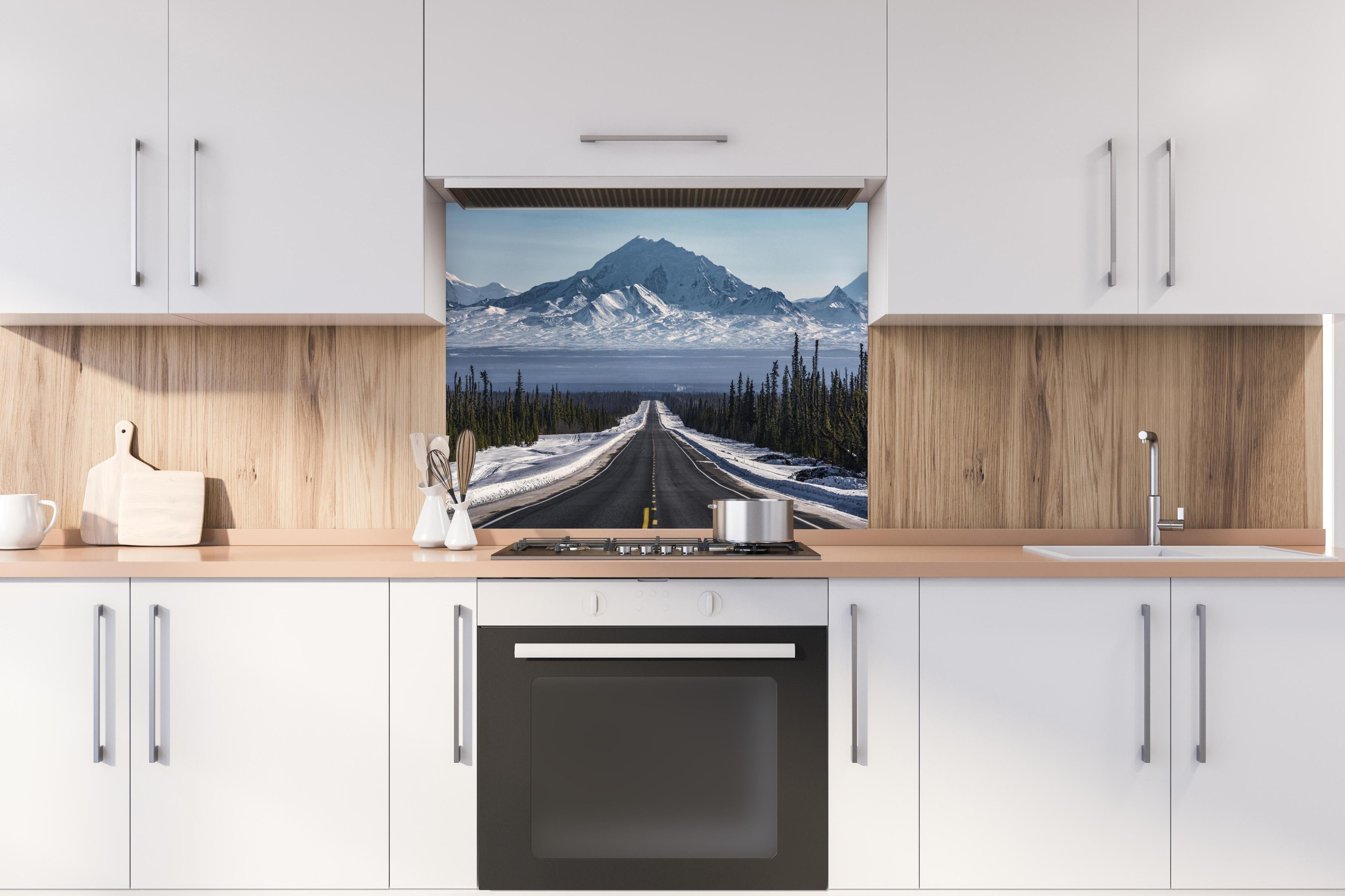 Spritzschutz - Verschneite Alpenstraße Alaska in Winterlandschaft hinter einem Cerankochfeld zwischen Holz-Kochutensilien
