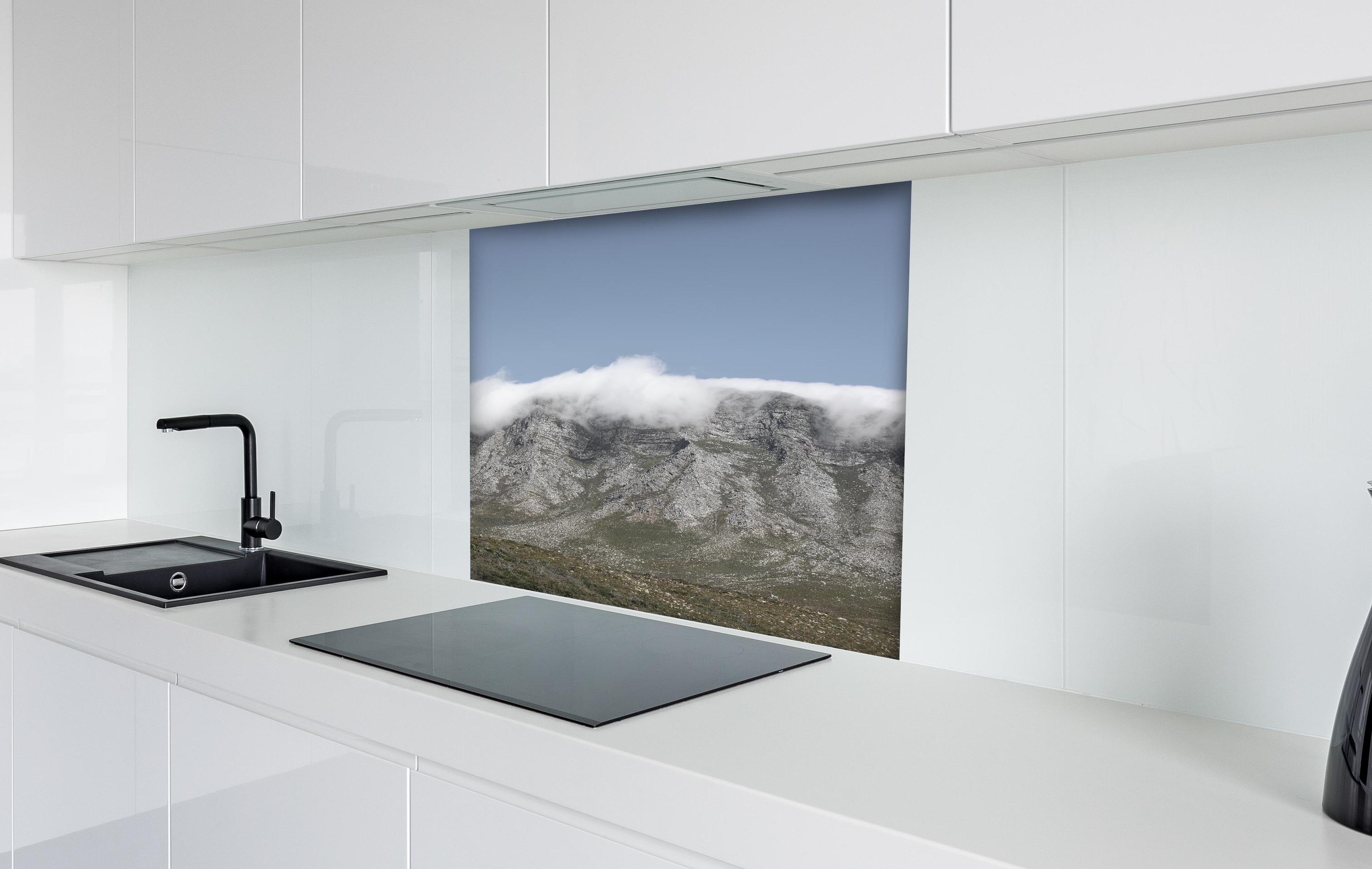 Spritzschutz - Verträumte Berglandschaft mit Wolkenverhang hinter einem Cerankochfeld zwischen Holz-Kochutensilien
