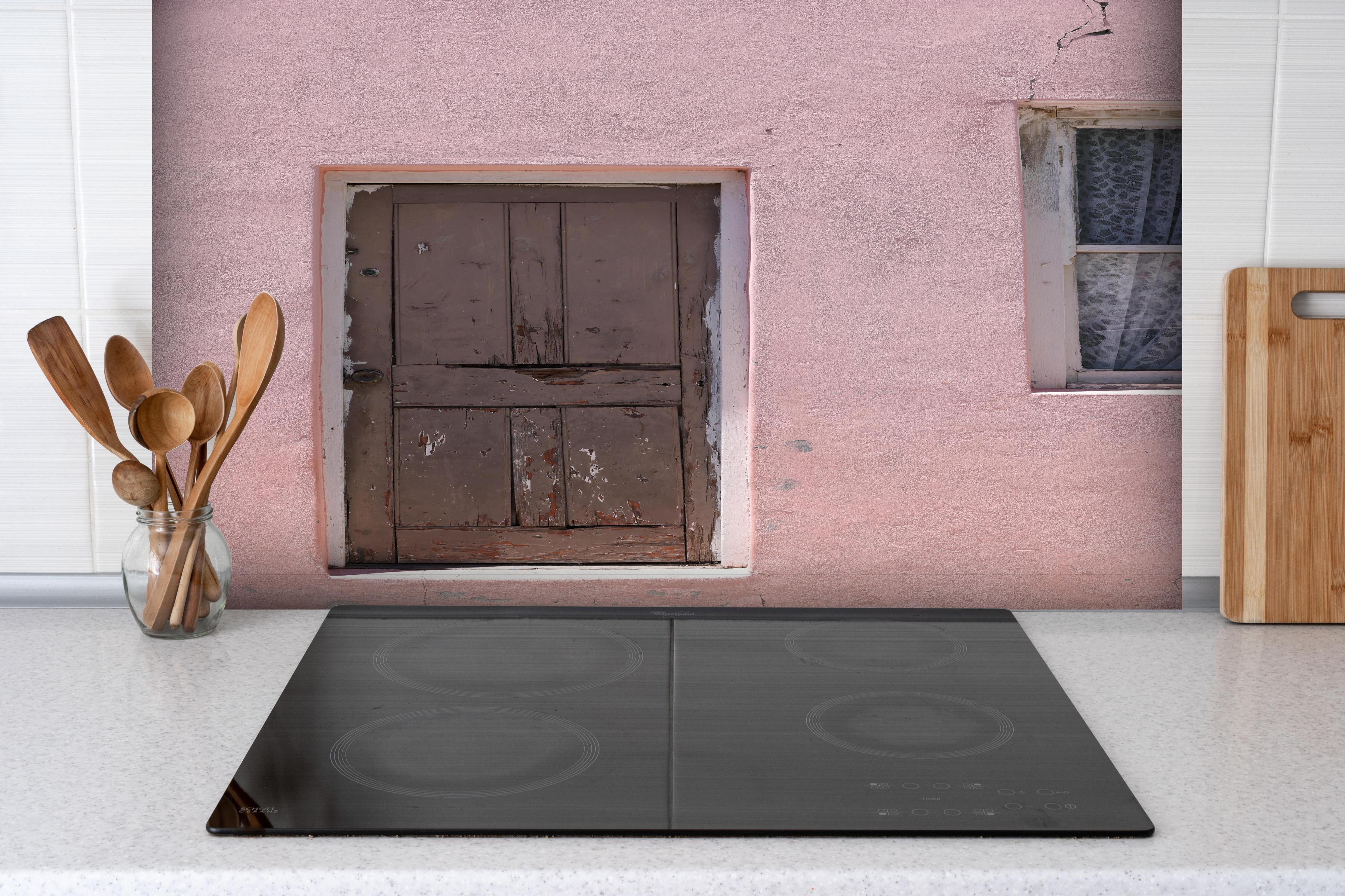 Spritzschutz - Verwitterte Holztür an rosa Bauernhaus hinter einem Cerankochfeld zwischen Holz-Kochutensilien
