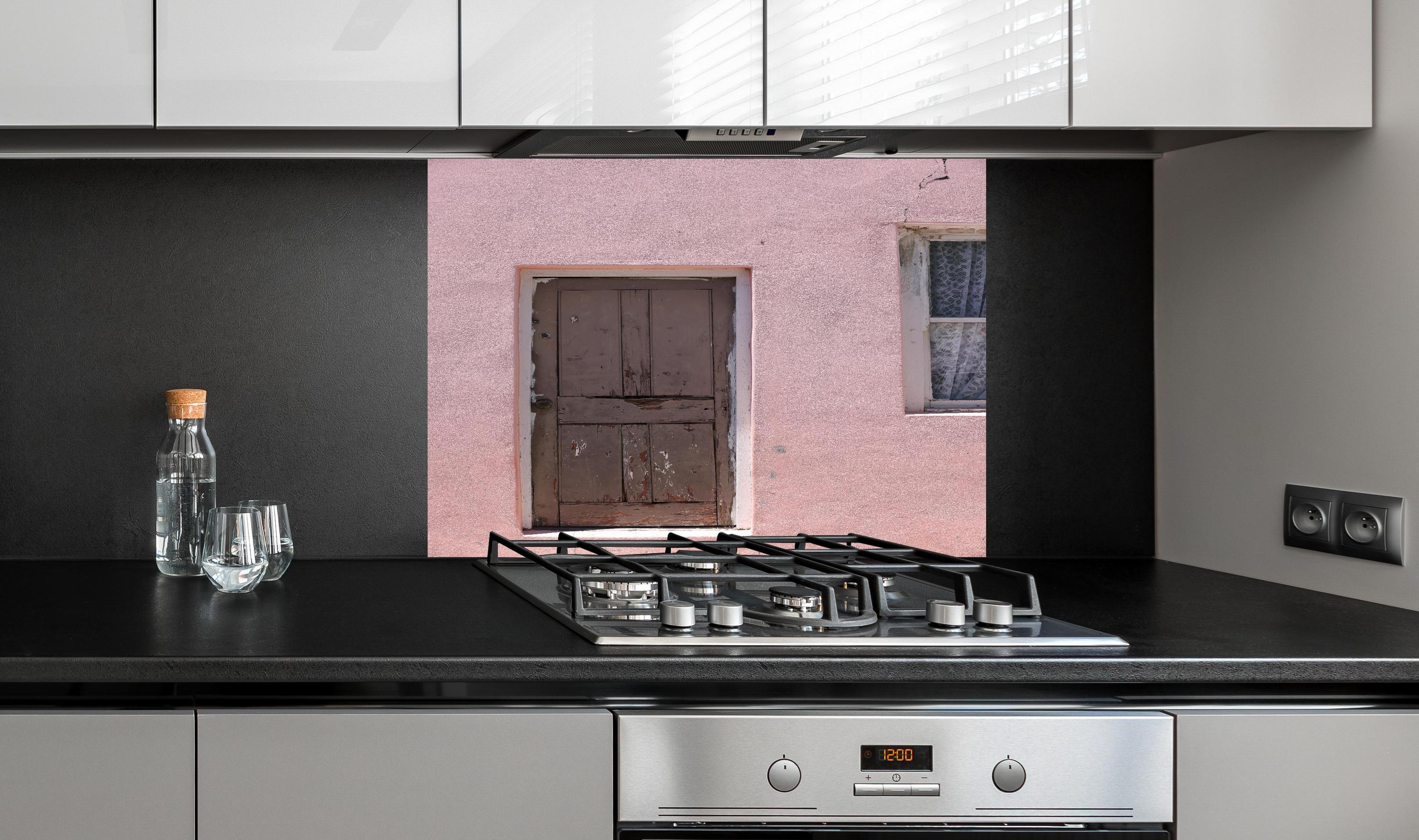 Spritzschutz - Verwitterte Holztür an rosa Bauernhaus hinter einem Cerankochfeld zwischen Holz-Kochutensilien
