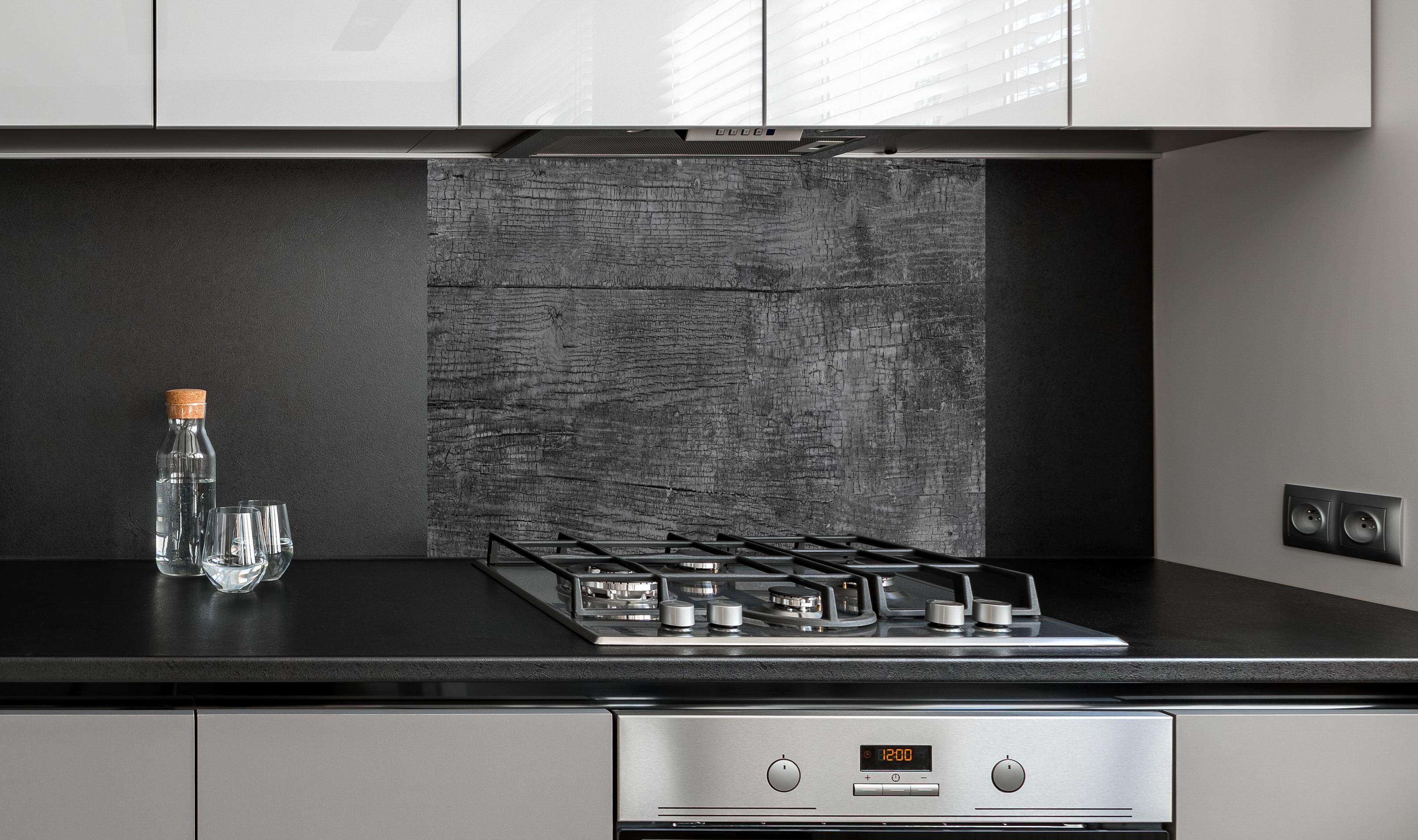 Spritzschutz - Vintage Schwarz-Graue Altholz-Textur hinter einem Cerankochfeld zwischen Holz-Kochutensilien
