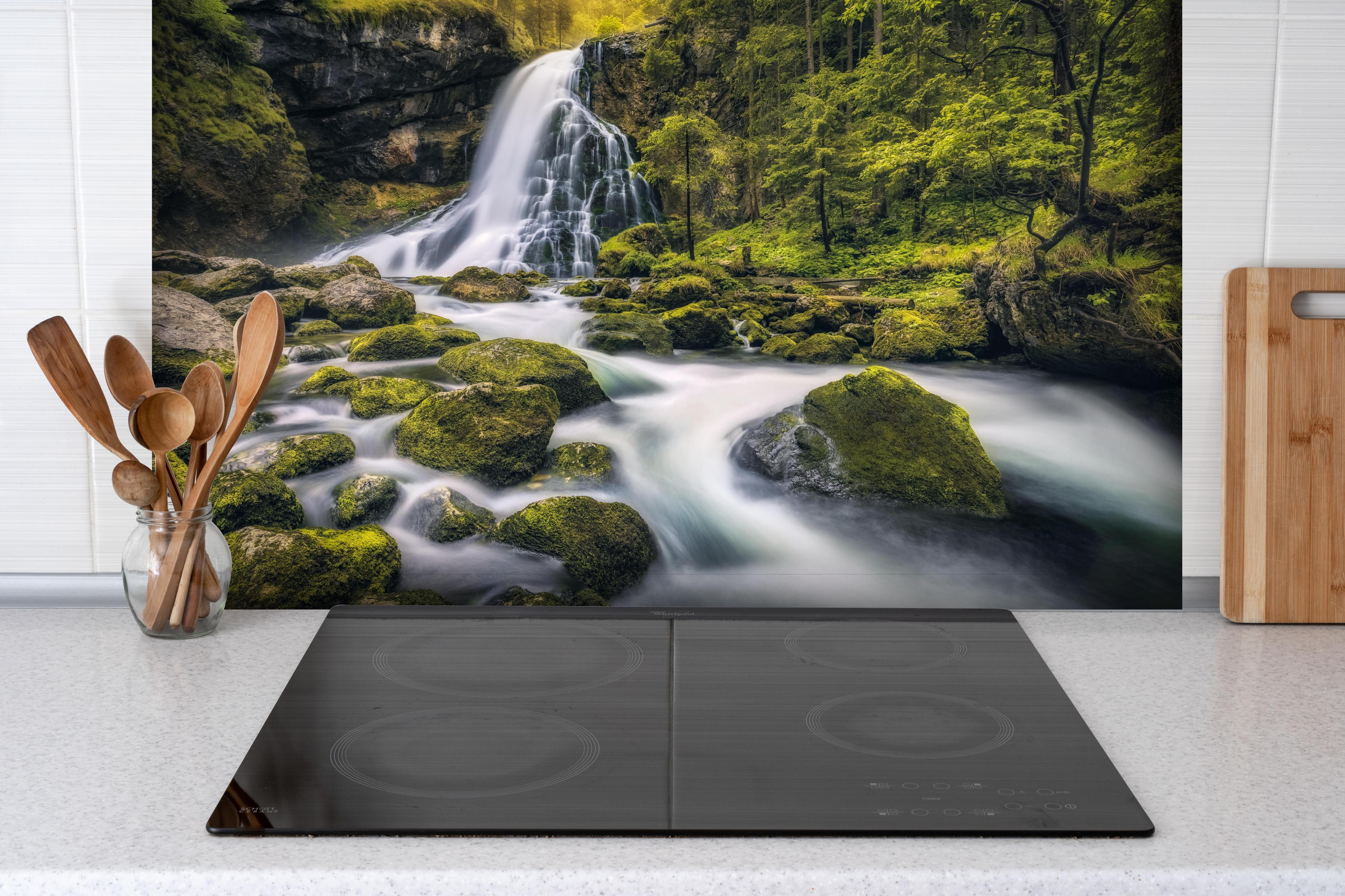 Spritzschutz - Wasserfall in Golling, Salzburg hinter einem Cerankochfeld zwischen Holz-Kochutensilien

