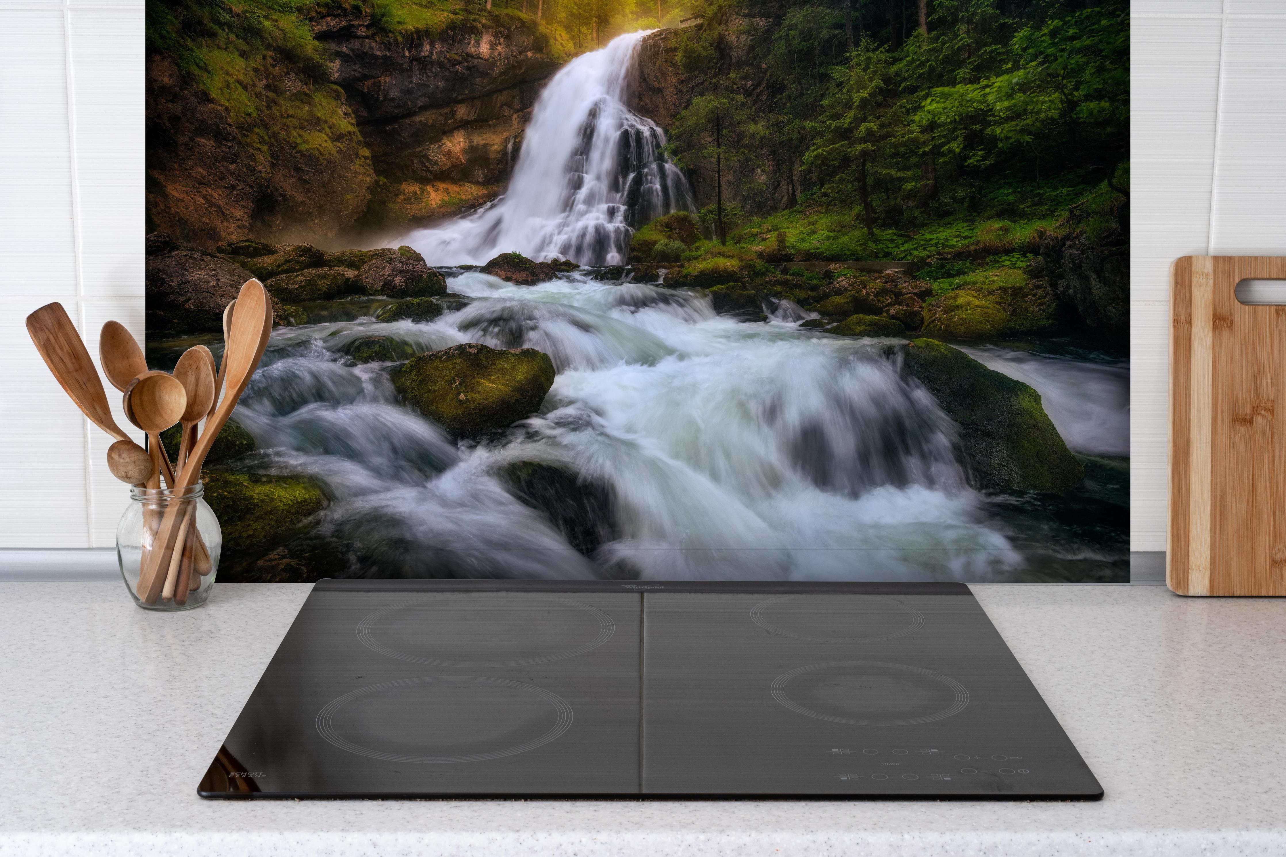 Spritzschutz - Wasserfall in bergiger Region hinter einem Cerankochfeld zwischen Holz-Kochutensilien
