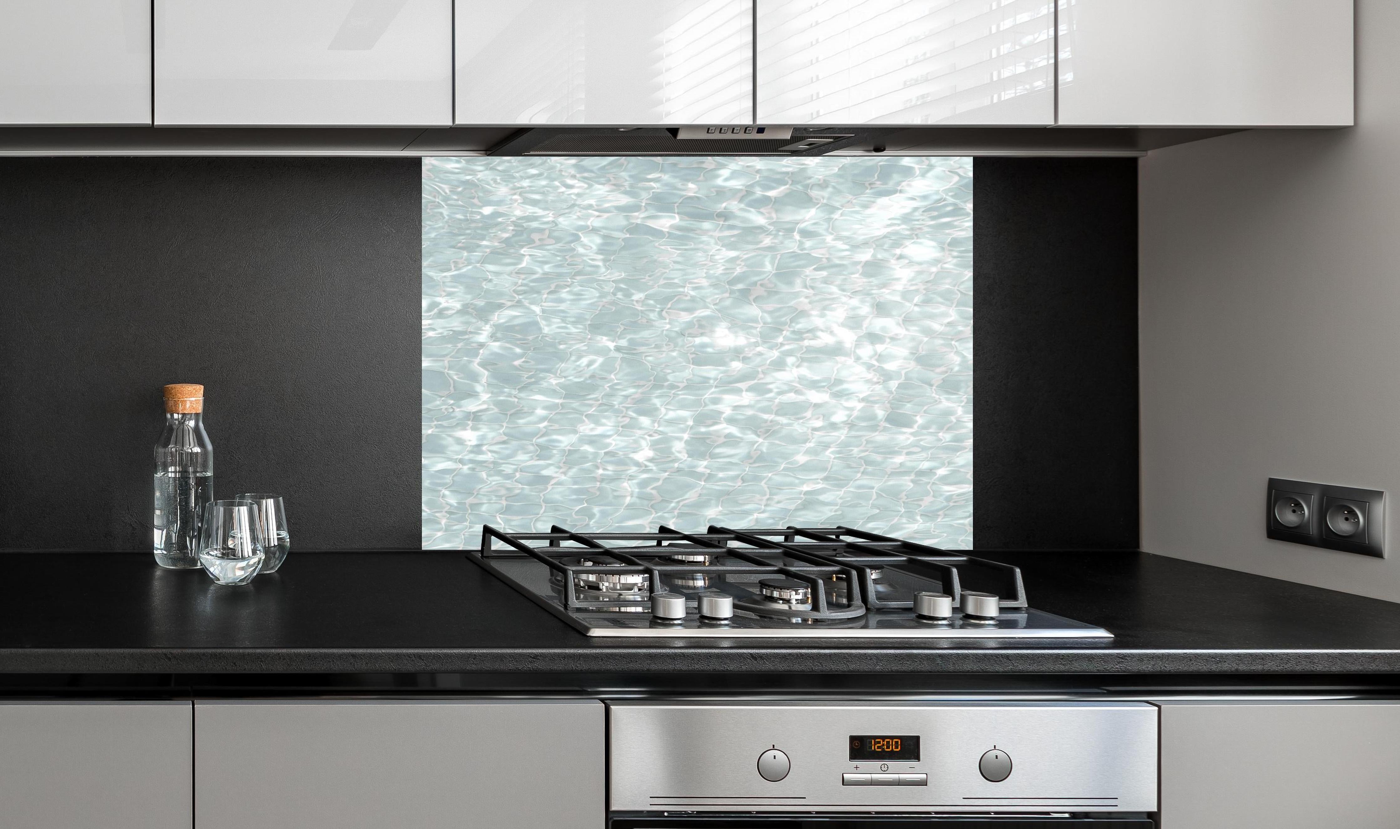 Spritzschutz - Wasseroberfläche hinter einem Cerankochfeld zwischen Holz-Kochutensilien
