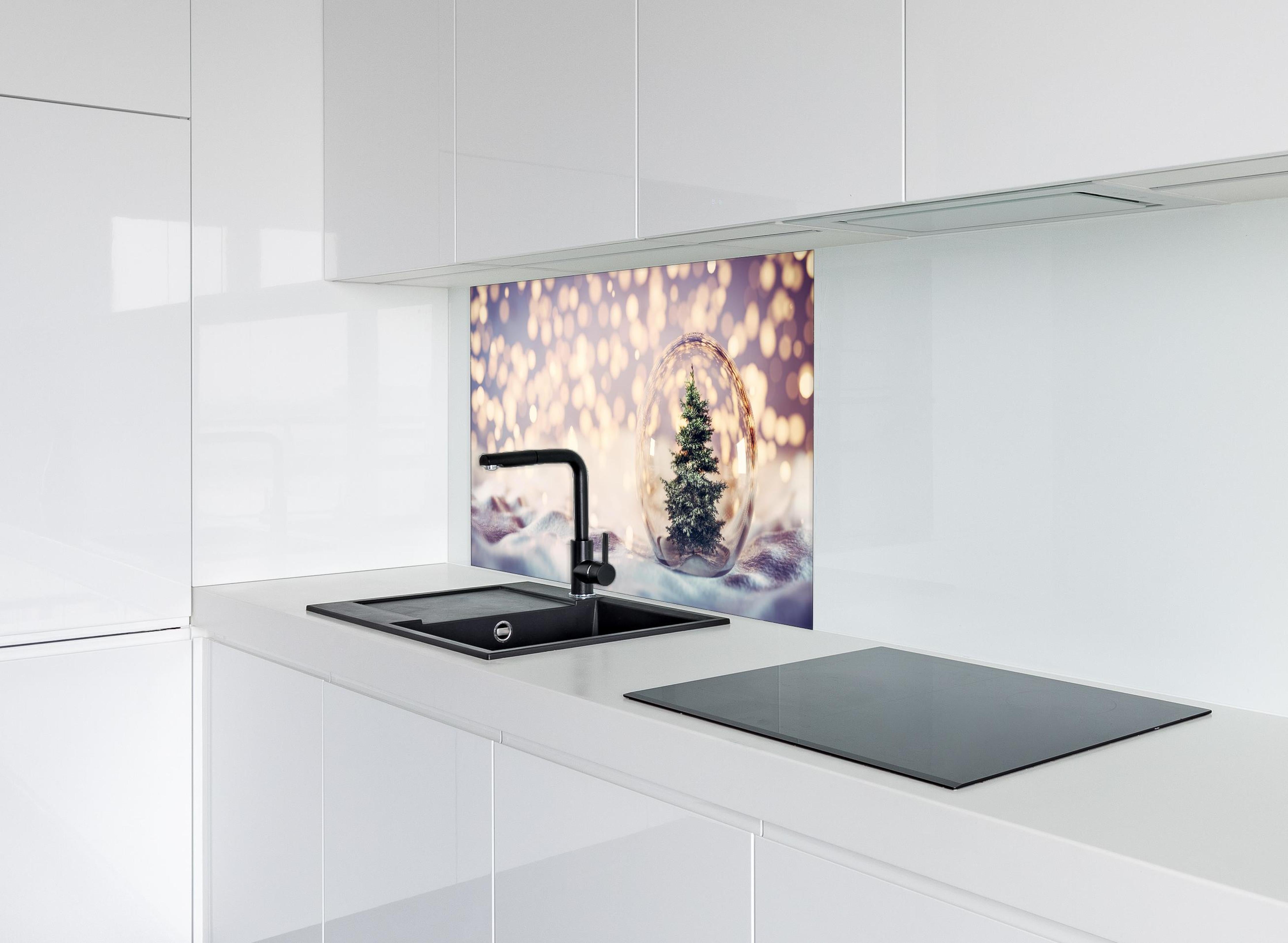 Spritzschutz - Weihnachtsbaum in einer Glaskugel hinter einem Cerankochfeld zwischen Holz-Kochutensilien
