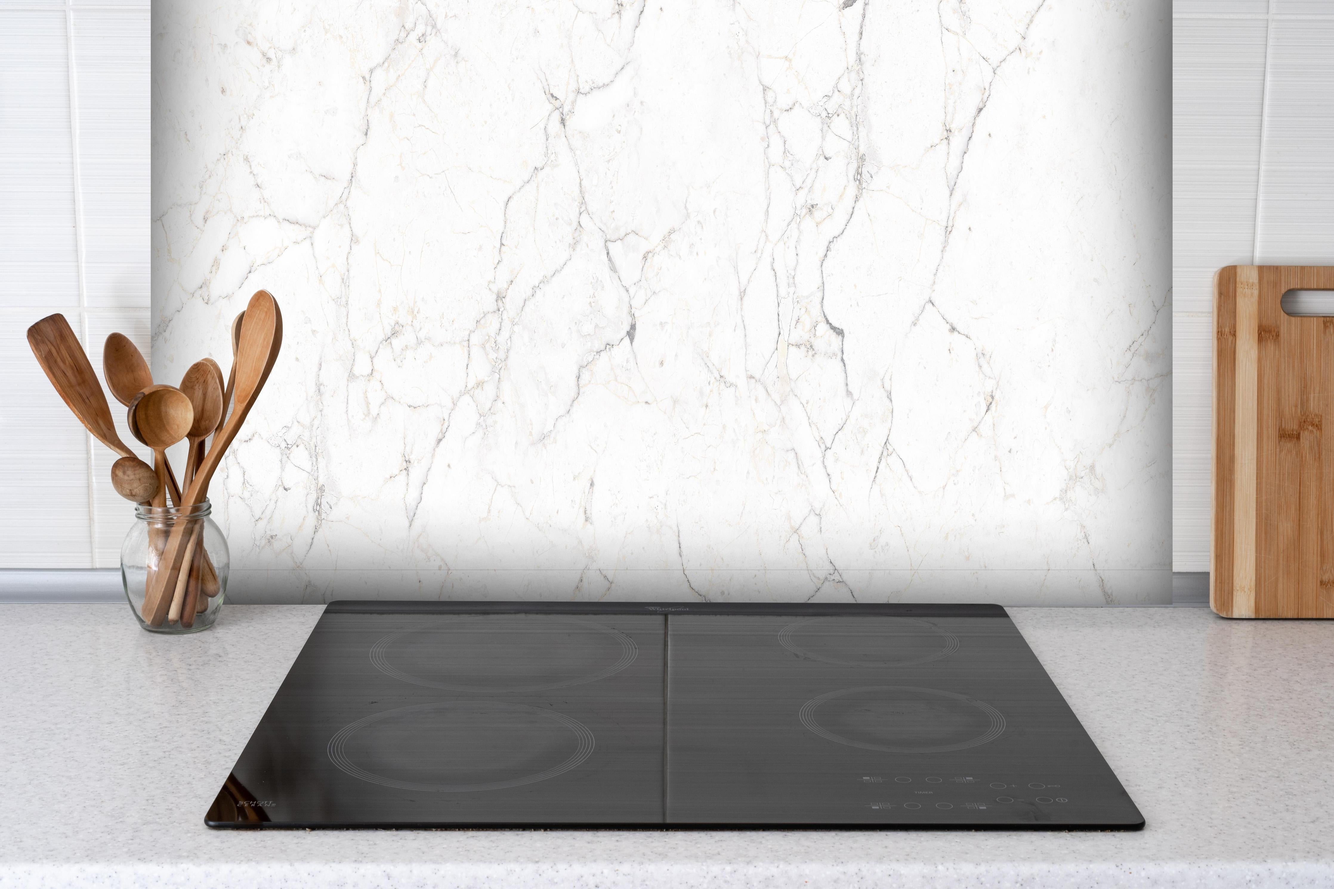 Spritzschutz - Weiße Marmor - Beton Textur hinter einem Cerankochfeld zwischen Holz-Kochutensilien
