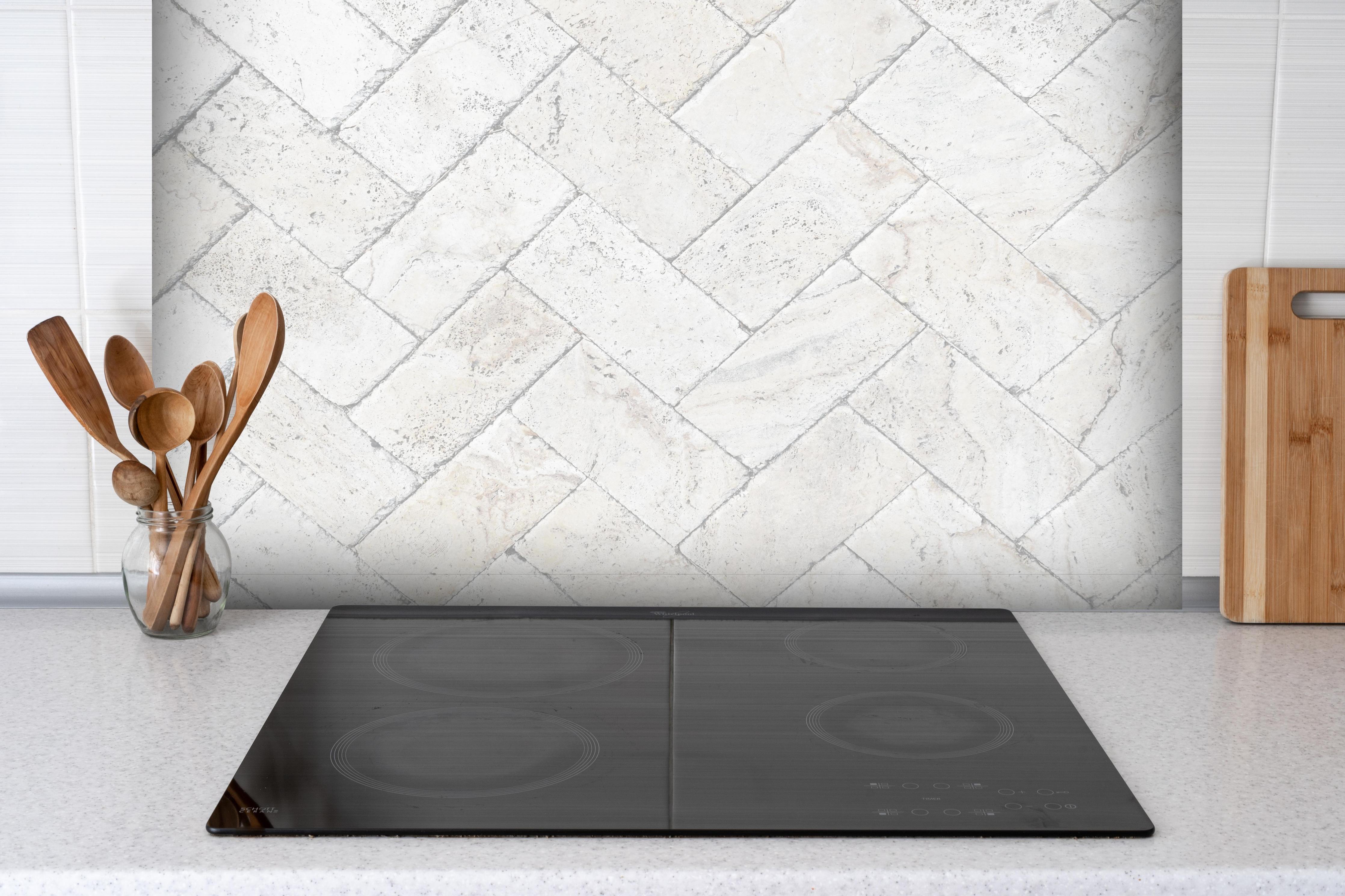 Spritzschutz - Weiße Pflastersteine hinter einem Cerankochfeld zwischen Holz-Kochutensilien
