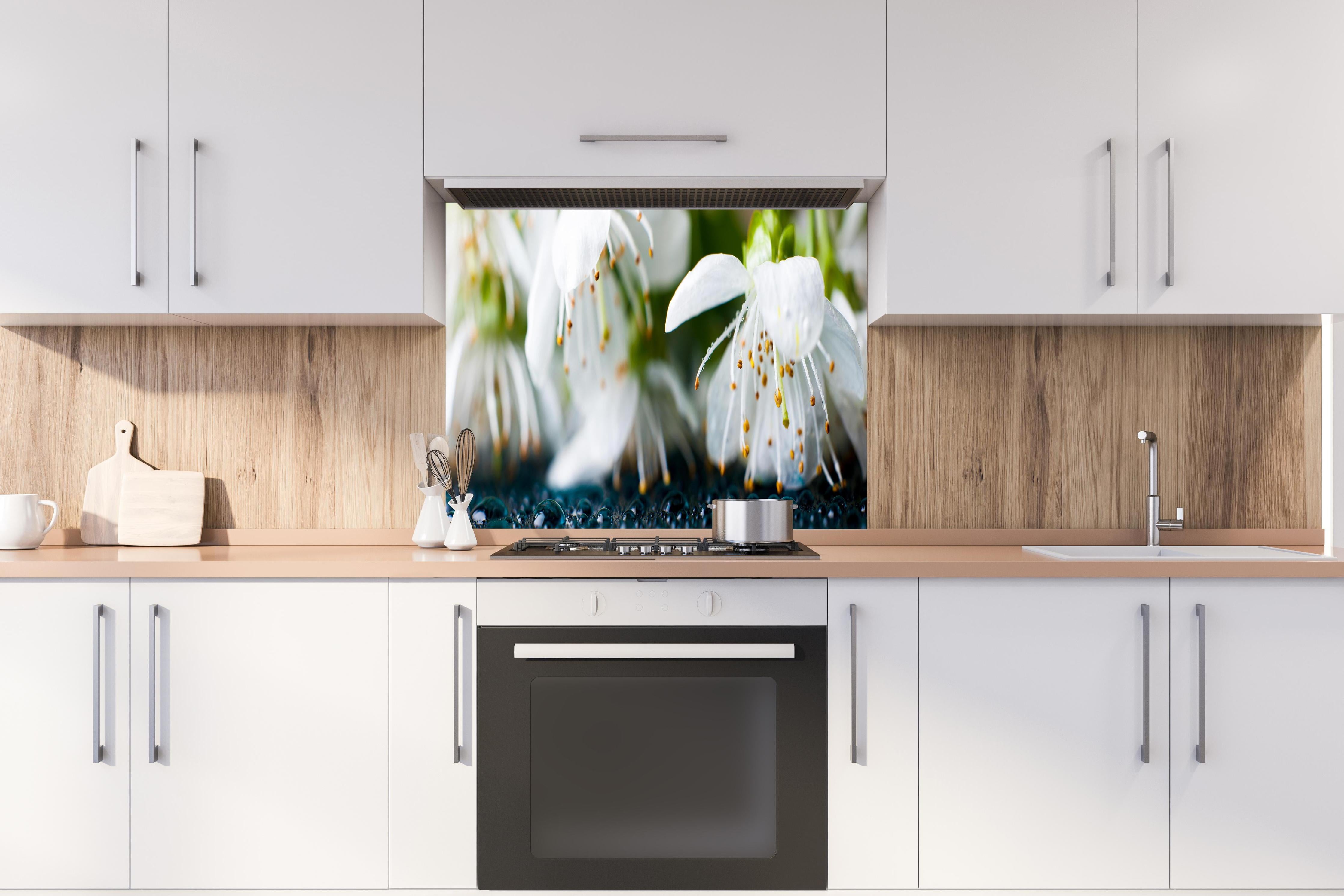 Spritzschutz - Weiße blühende Frühlingsblumen hinter einem Cerankochfeld zwischen Holz-Kochutensilien
