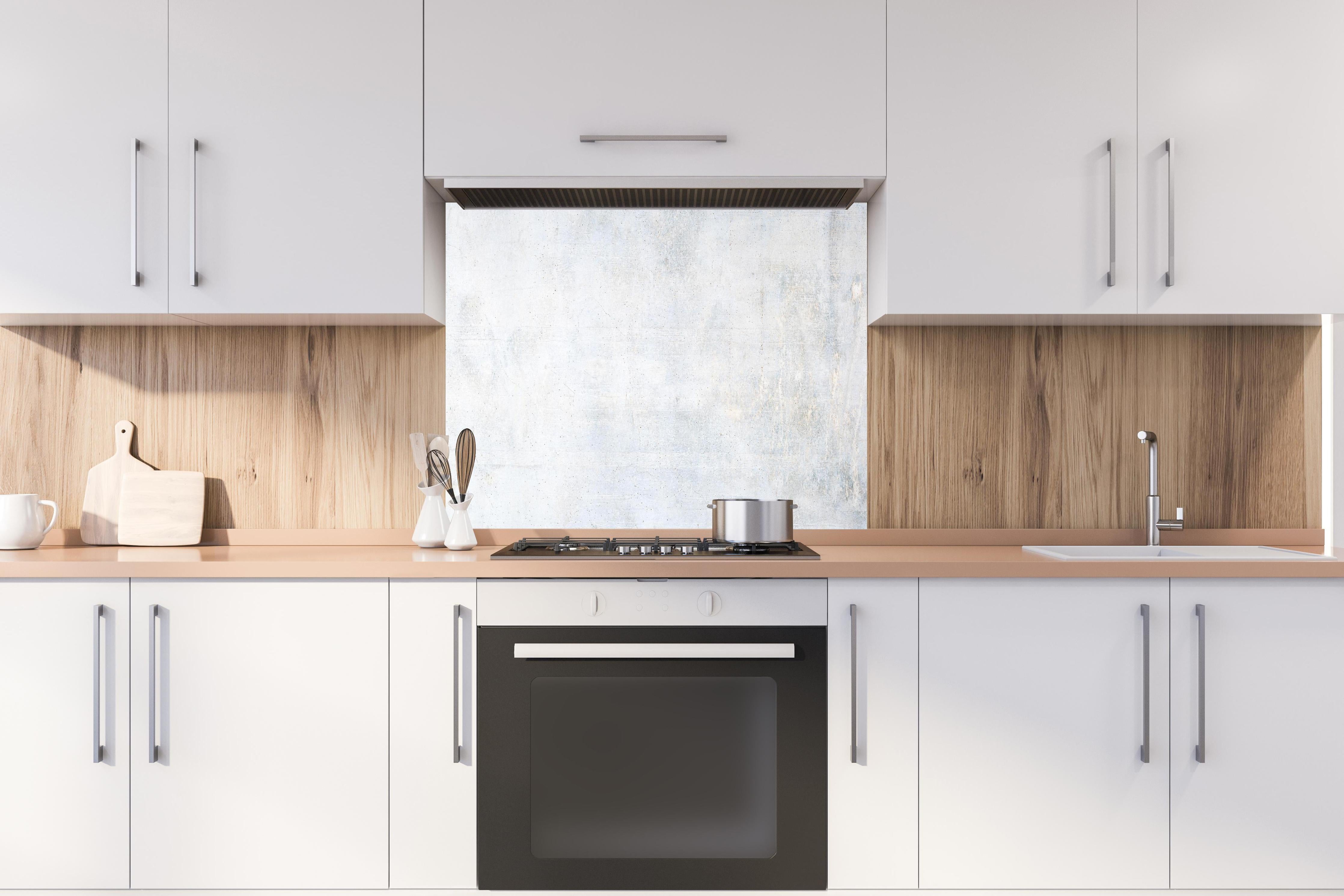 Spritzschutz - Weiße verwitterte Betonwand hinter einem Cerankochfeld zwischen Holz-Kochutensilien
