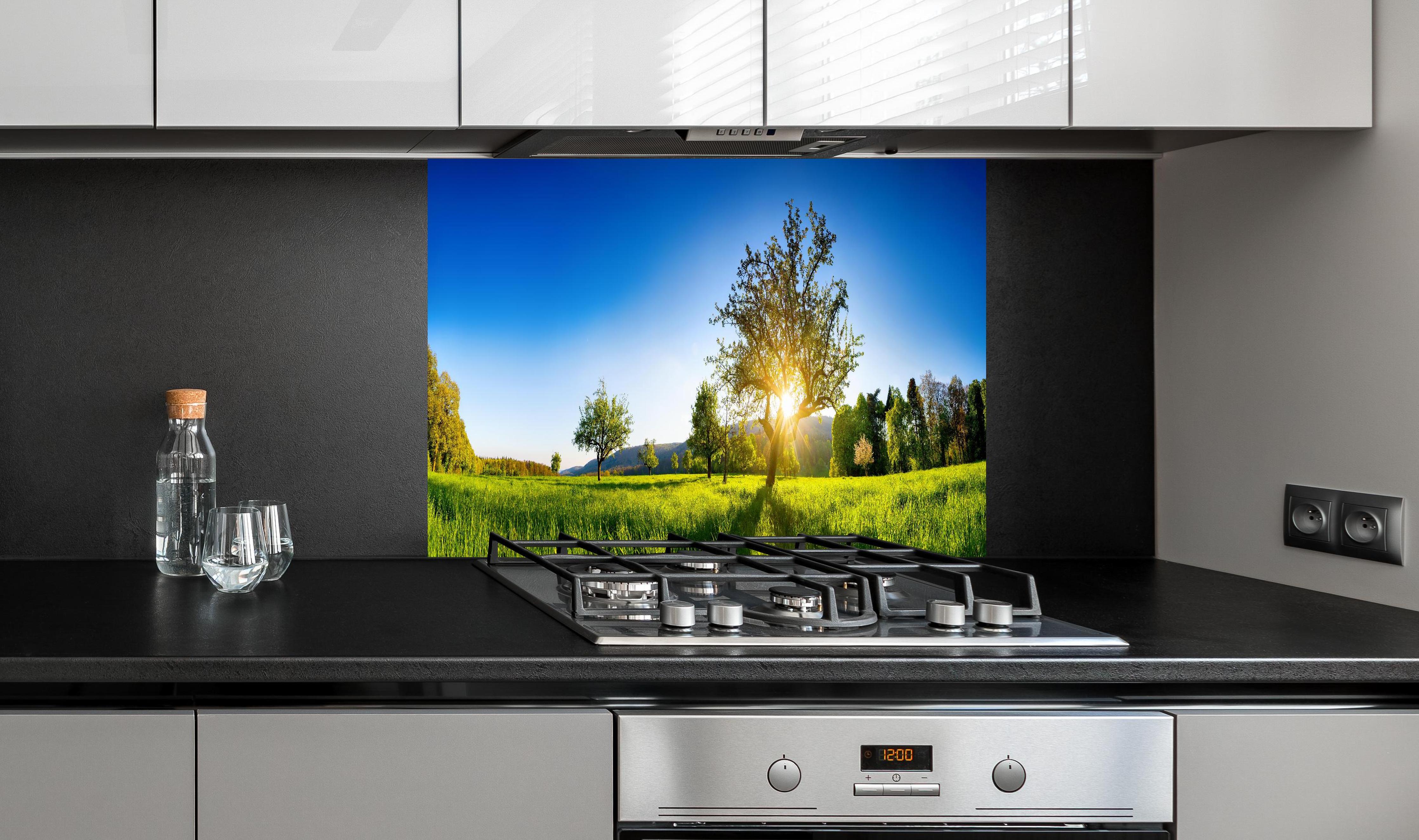 Spritzschutz - Weite Landschaft unter klarem blauem Himmel hinter einem Cerankochfeld zwischen Holz-Kochutensilien
