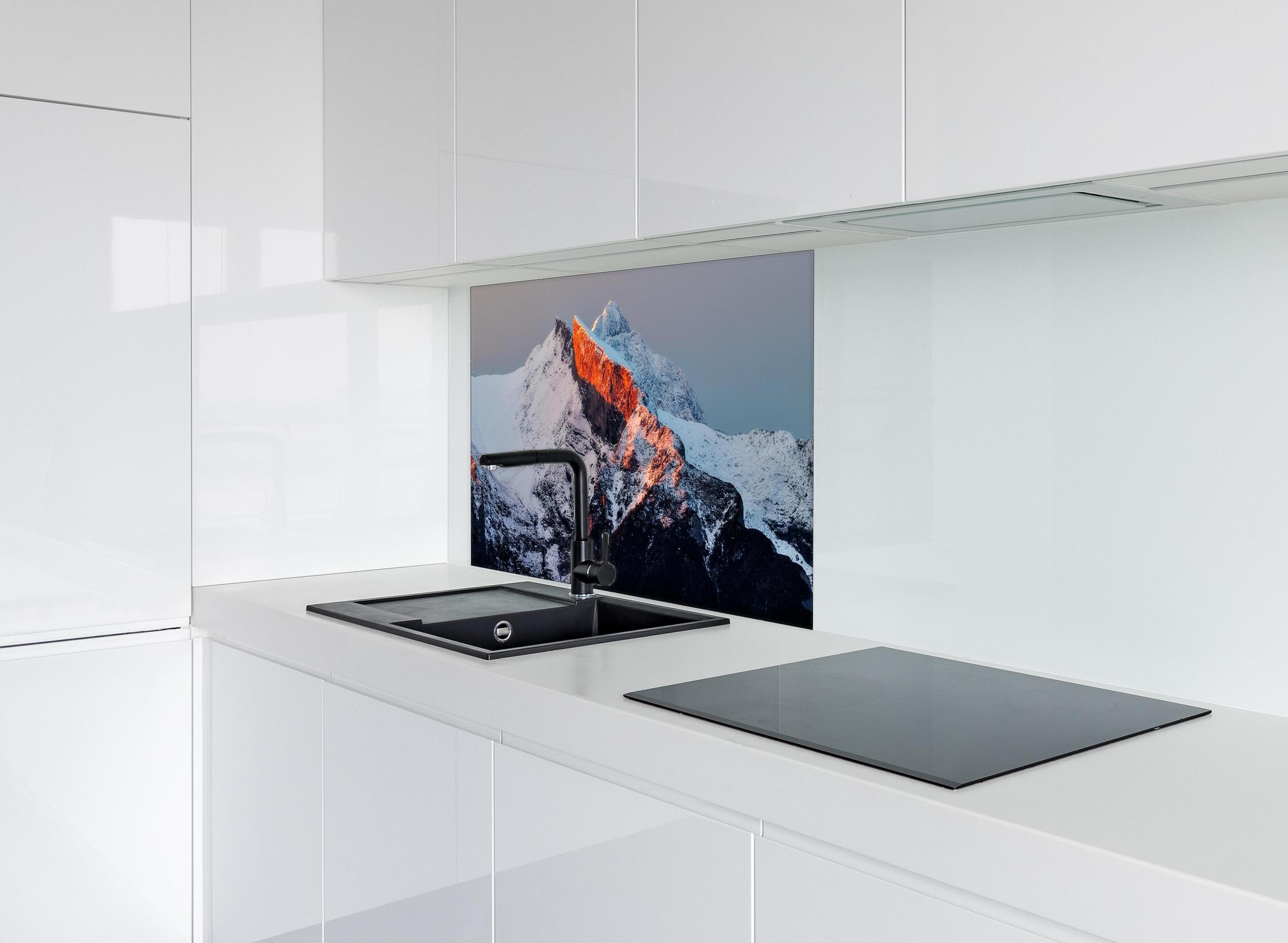 Spritzschutz - Winterlicher Sonnenaufgang über schneebedeckten Gipfeln hinter einem Cerankochfeld zwischen Holz-Kochutensilien
