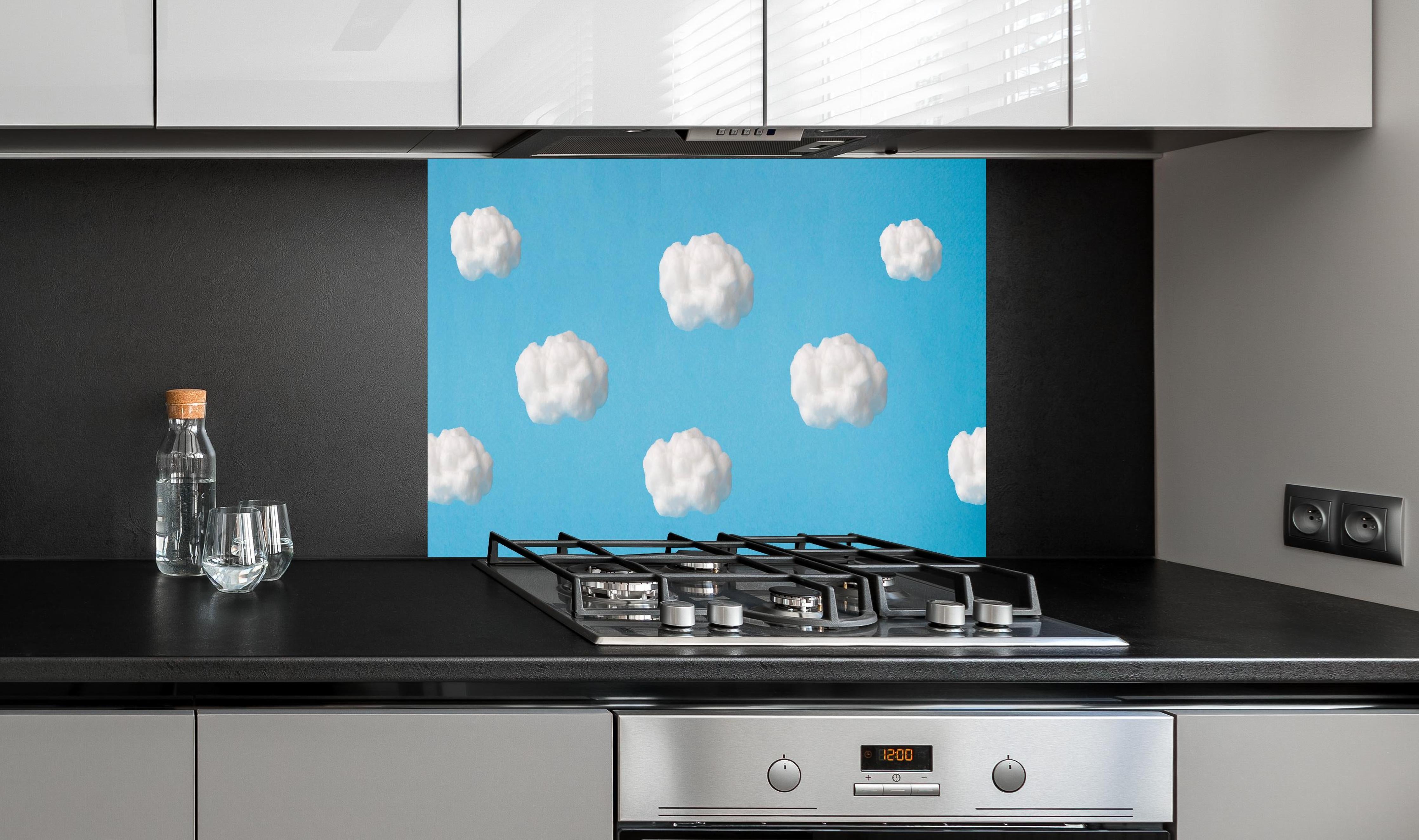 Spritzschutz - Wolke aus Watte auf himmelblauem Hintergrund hinter einem Cerankochfeld zwischen Holz-Kochutensilien
