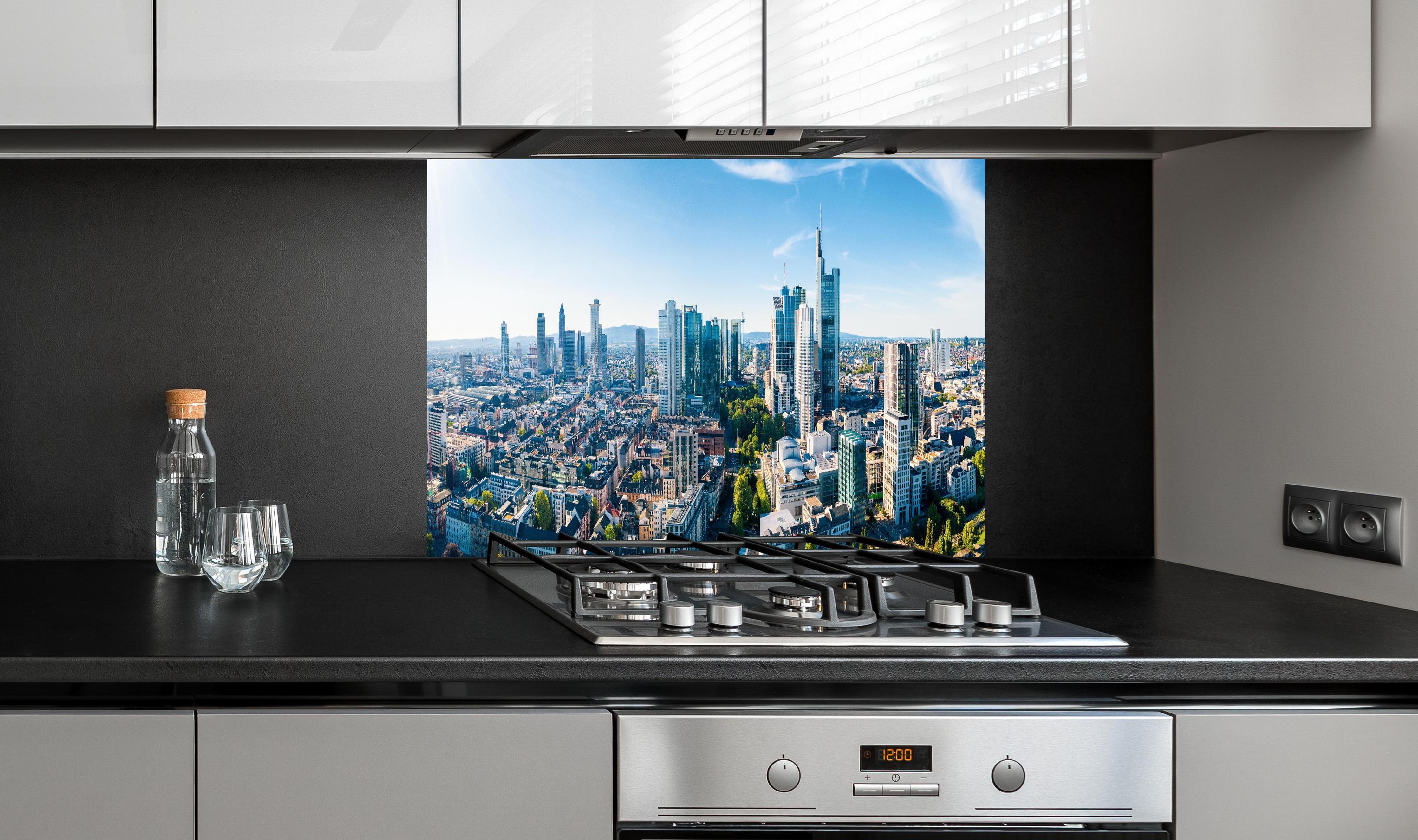 Spritzschutz - Wolkenkratzer -  Frankfurt am Main hinter einem Cerankochfeld zwischen Holz-Kochutensilien
