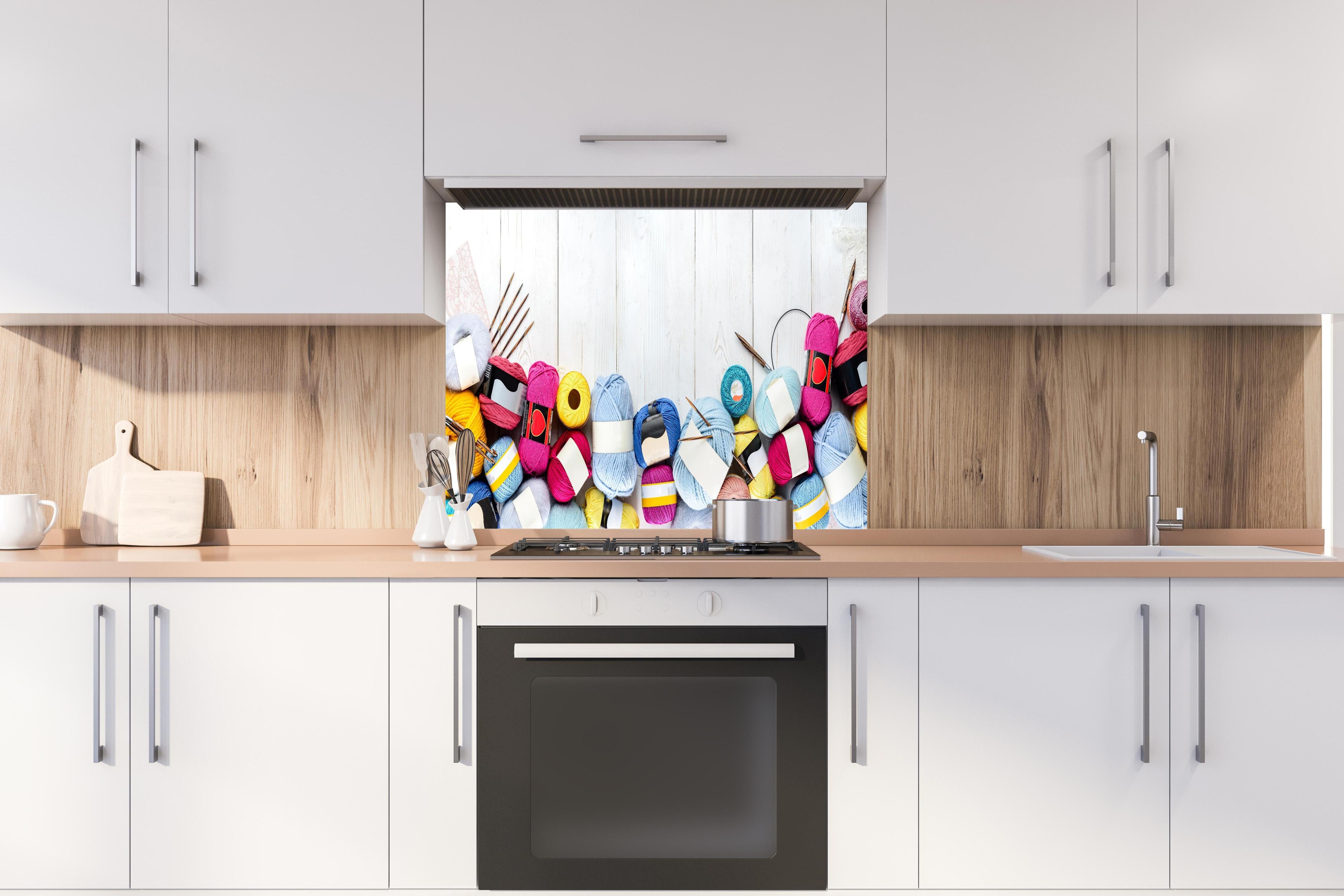 Spritzschutz - Wolle und Stricknadeln auf Holzhintergrund hinter einem Cerankochfeld zwischen Holz-Kochutensilien
